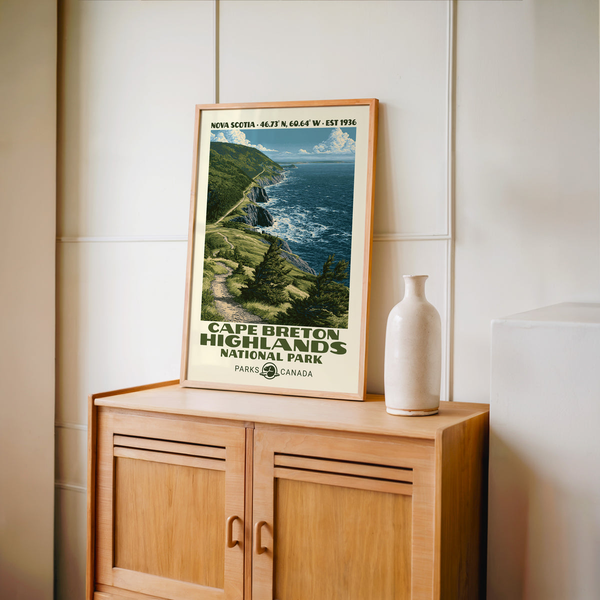 Nova Scotia cliff coast wall art in an oak frame on a light wood cabinet beside a stoneware vase