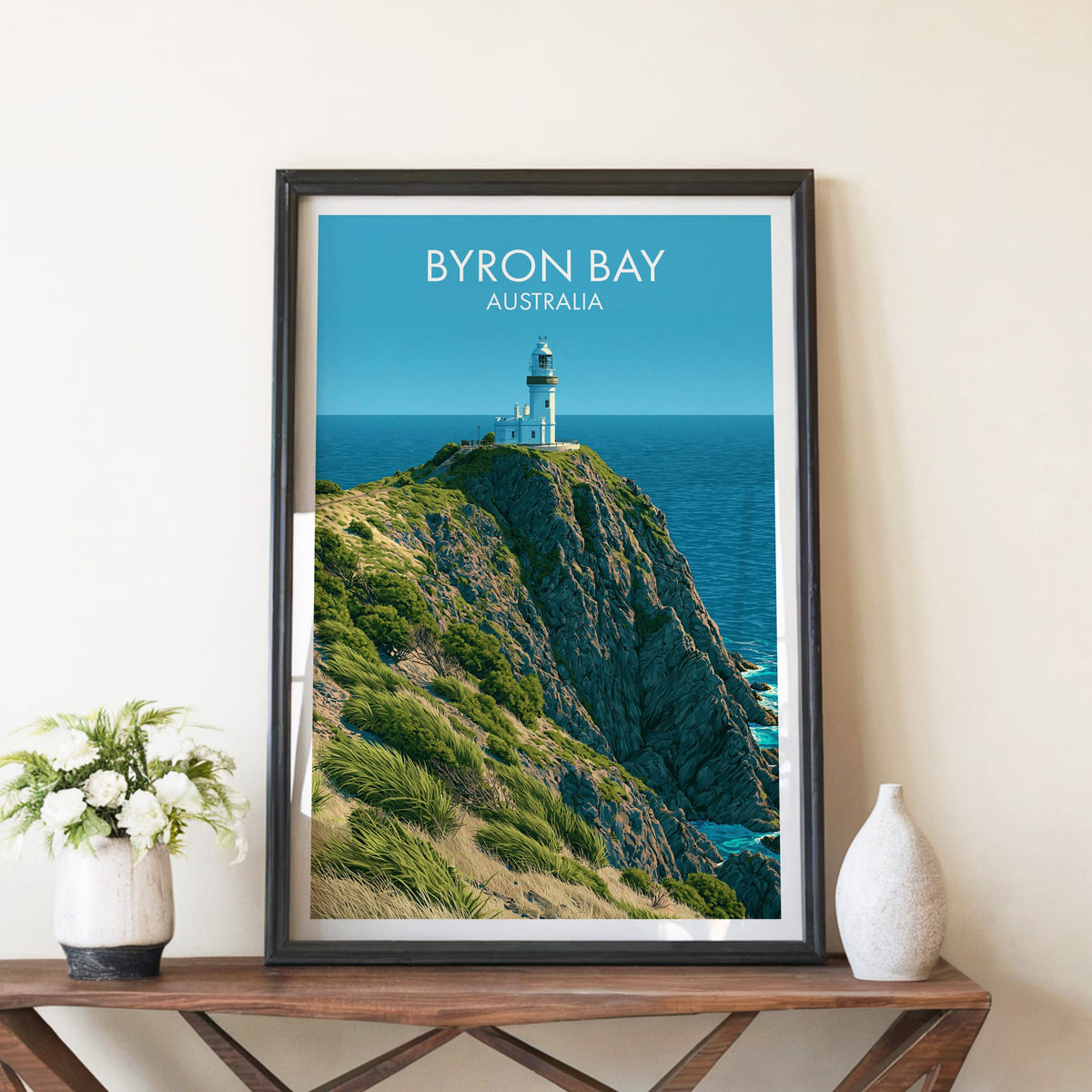 Byron Bay lighthouse poster in a black frame on a walnut console with white peonies and a tall stone vase