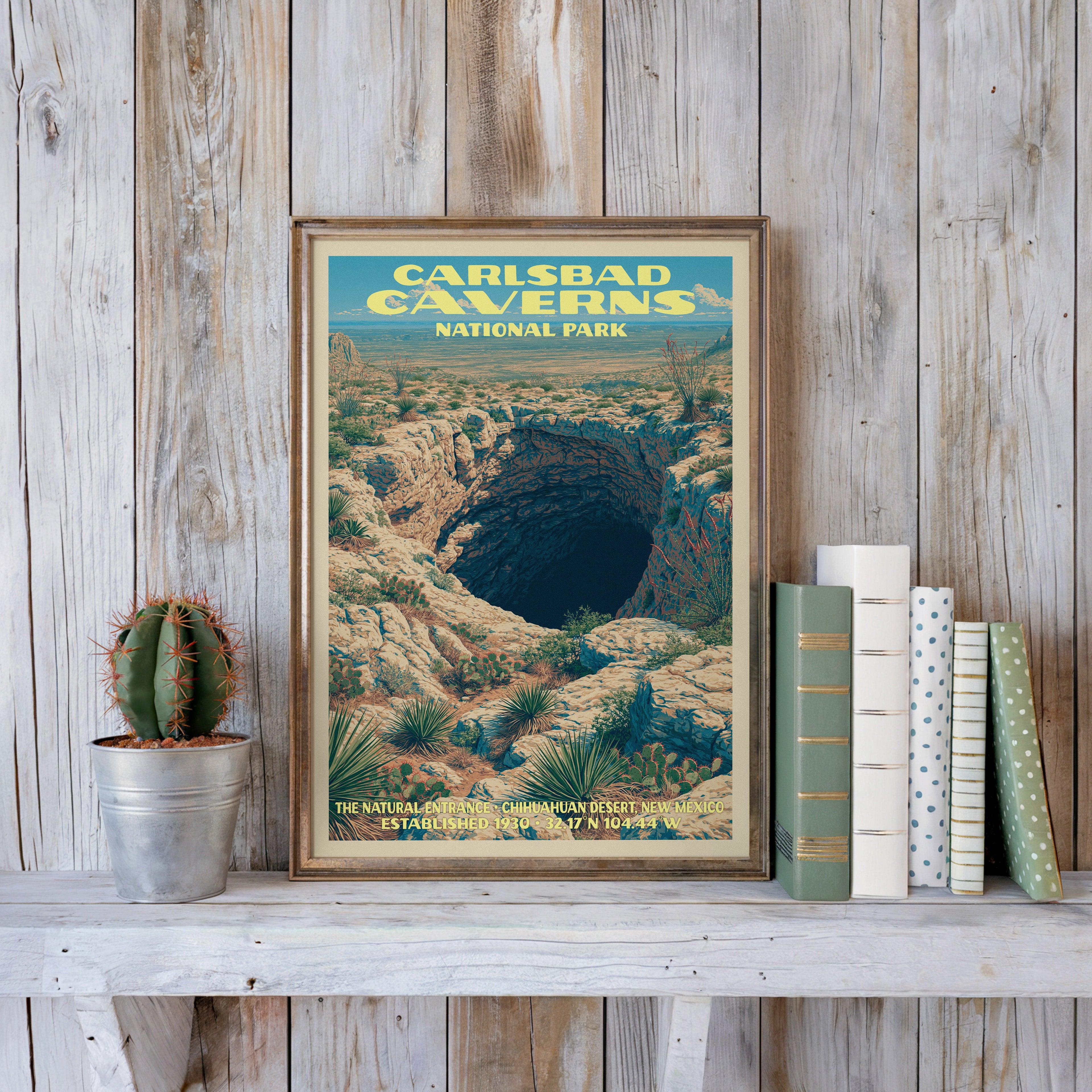 Carlsbad Caverns vintage poster in a slim gold frame on a whitewashed plank wall beside a cactus and pastel books