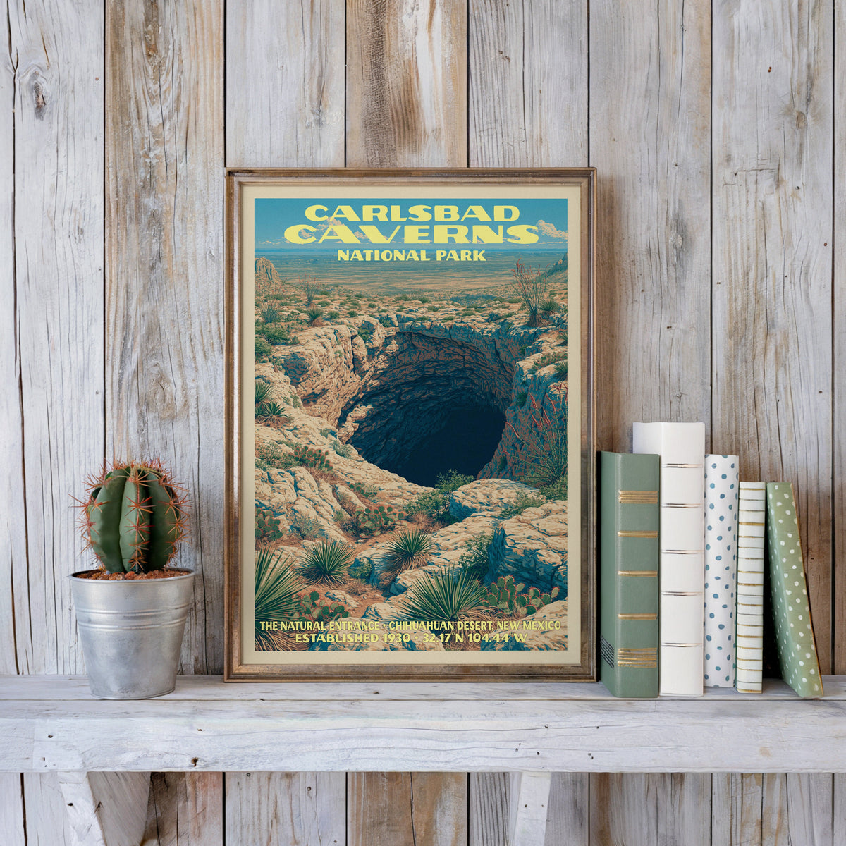 Carlsbad Caverns vintage poster in a slim gold frame on a whitewashed plank wall beside a cactus and pastel books