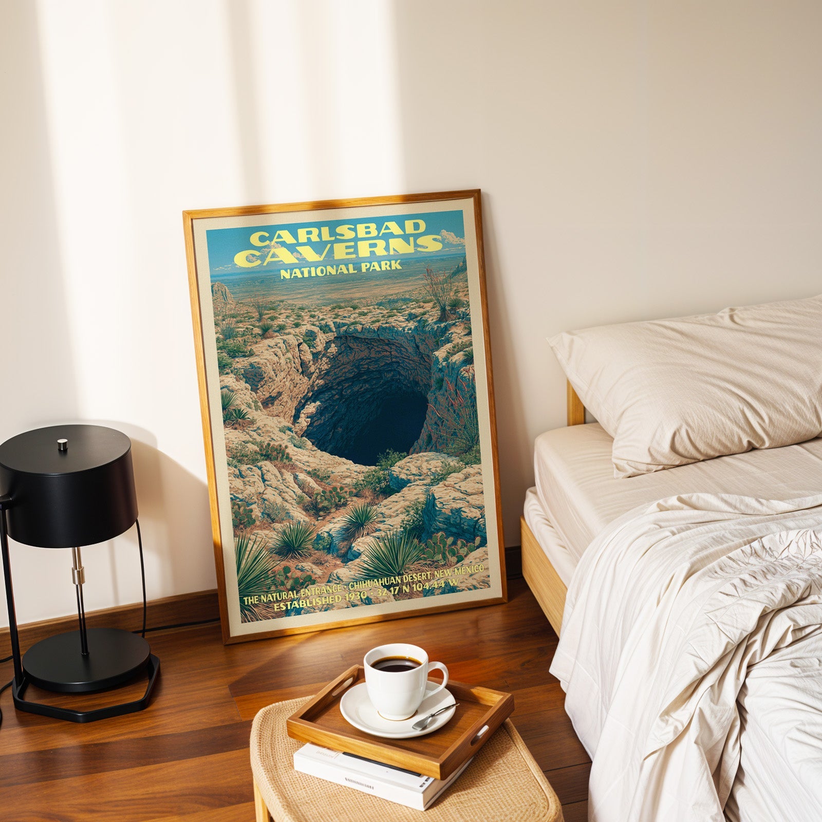 Natural Entrance Carlsbad Caverns poster in a gold frame on the floor beside a made bed and a black lamp