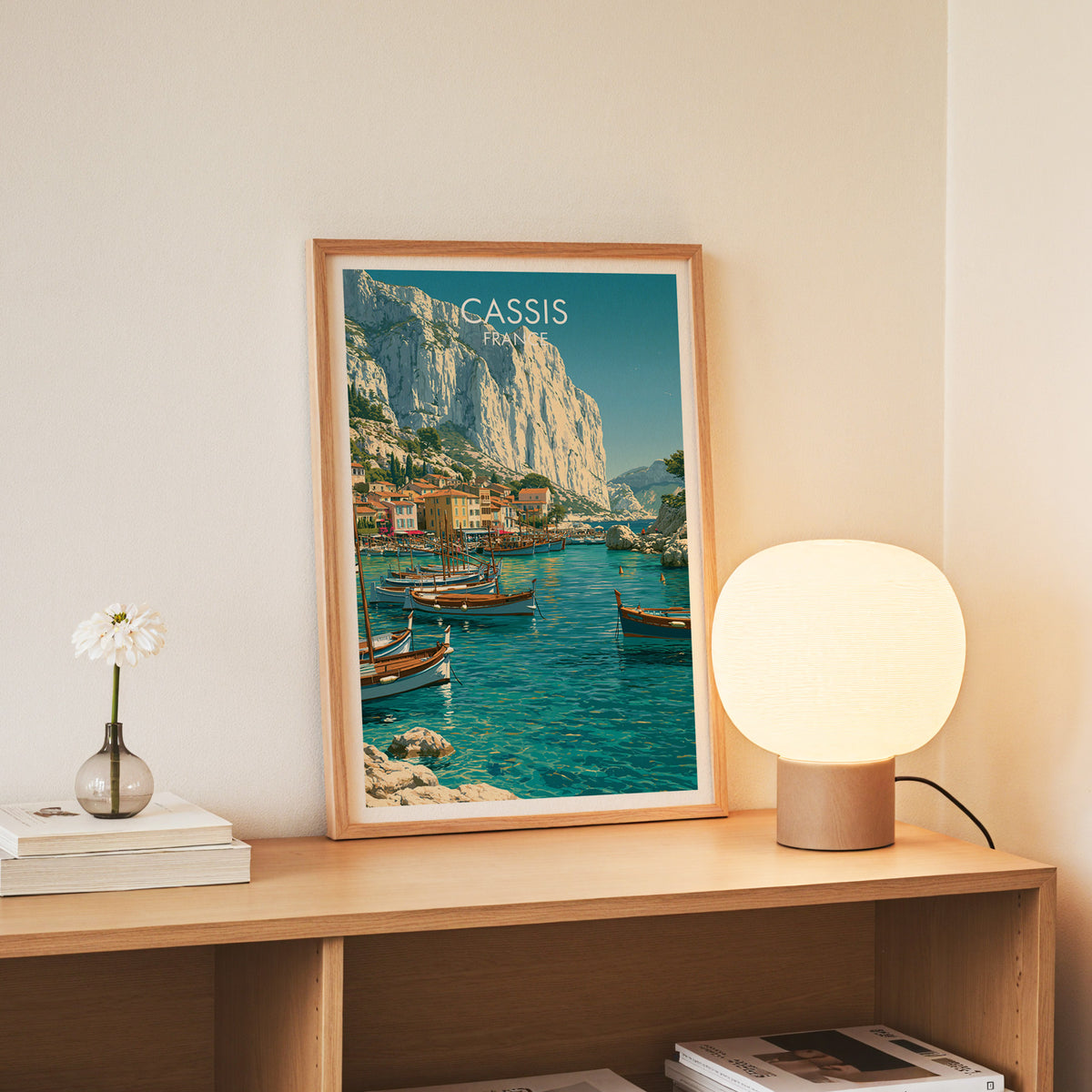 Cassis France wall art, slim oak frame standing on an oak console beside a daisy in a glass bottle
