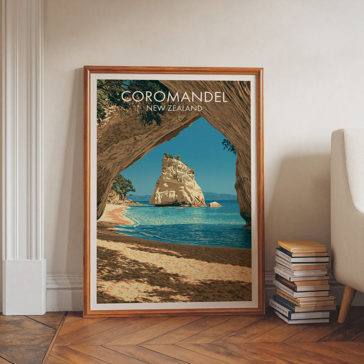 Turquoise cove seascape in a walnut frame on a herringbone floor beside stacked books and an armchair