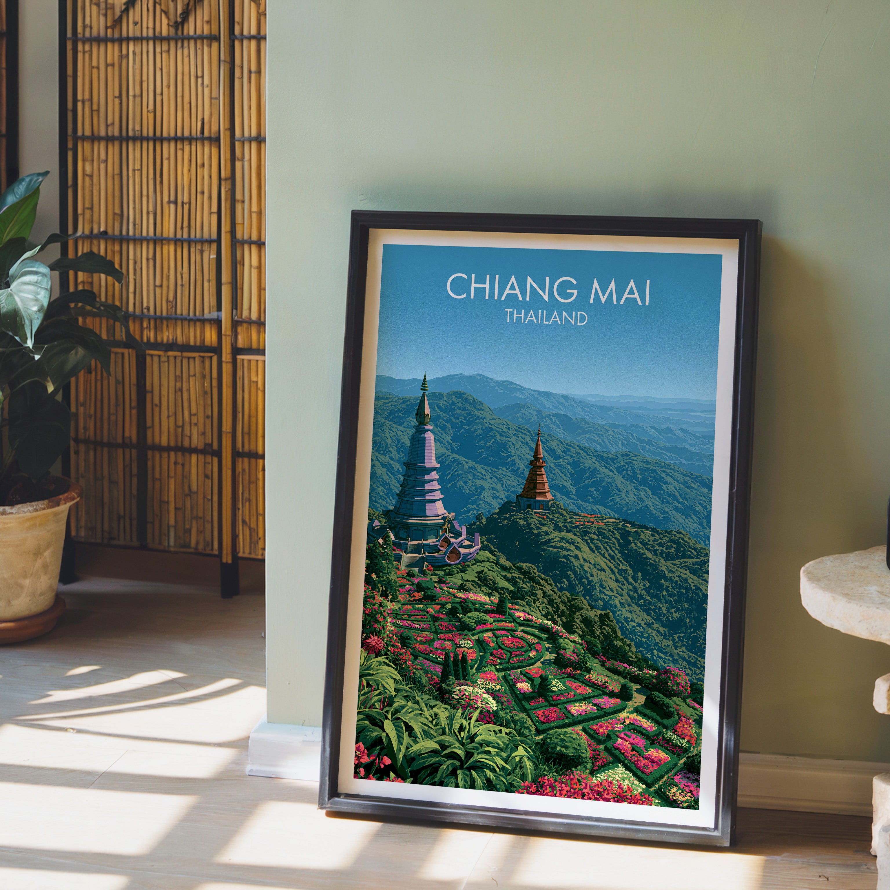 Chiang Mai Thailand wall art in a black frame leaning against a sage green wall beside a bamboo screen