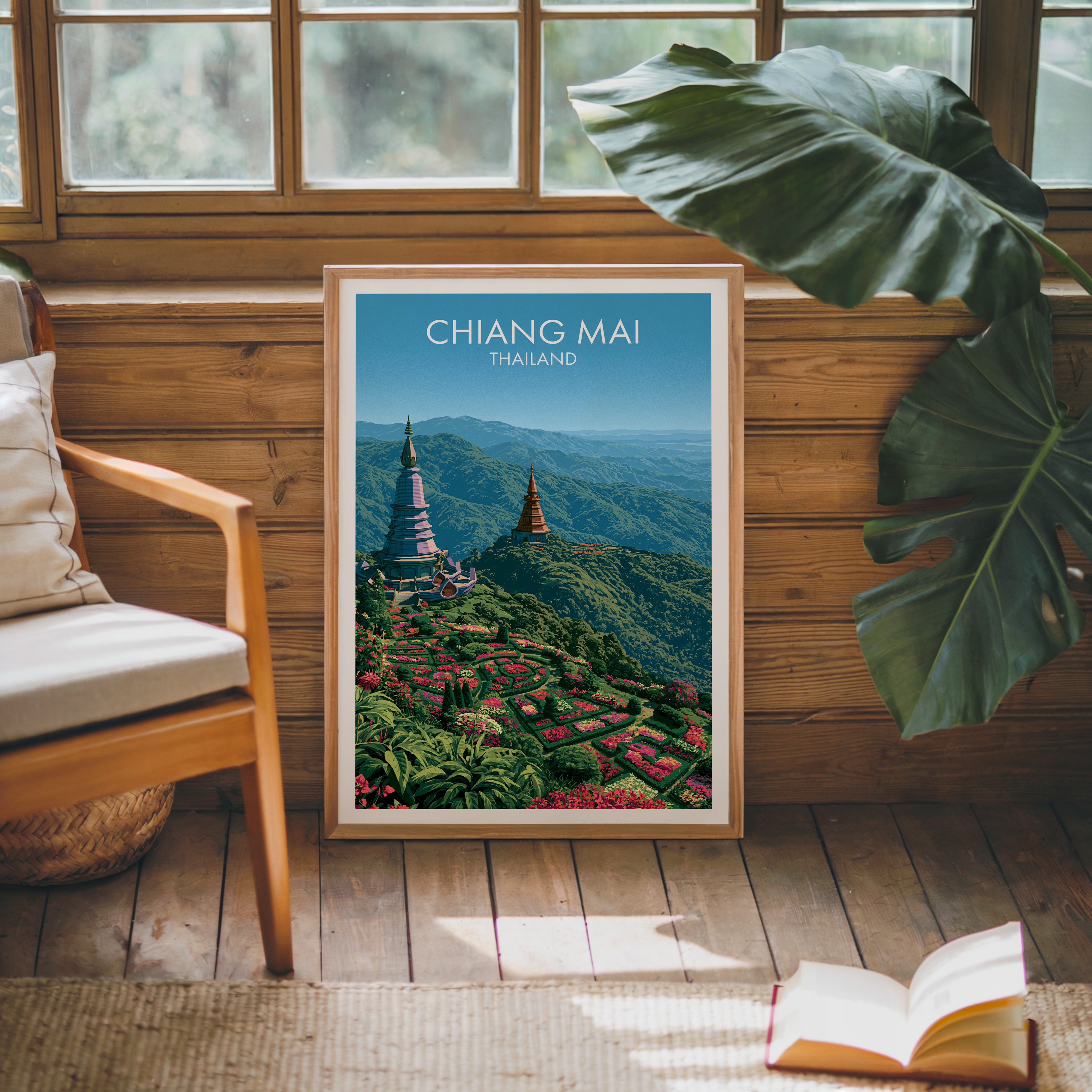 Framed Chiang Mai Thailand poster leaning against a timber cabin wall with monstera leaves and an open book