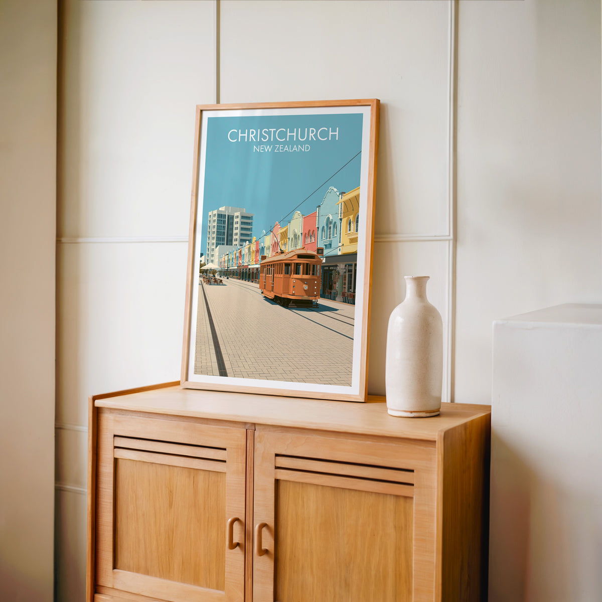 Pastel city street print in an oak frame on a light oak cabinet against a cream panelled wall