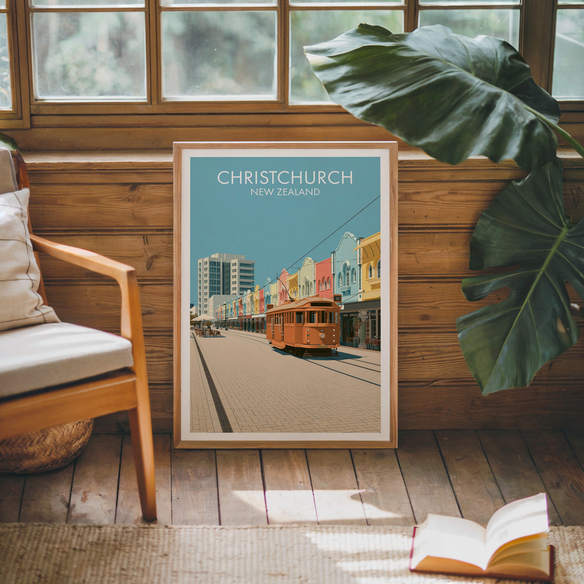 Tram street print leaning on a pine cabin wall beside a wooden armchair, monstera leaf and open book