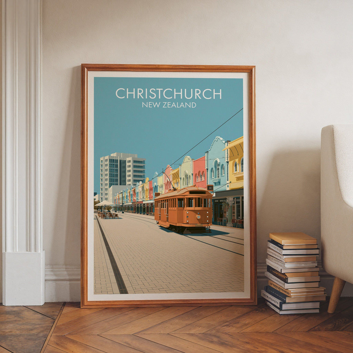 Orange tram artwork in a walnut frame on a herringbone floor beside stacked books and a pale armchair