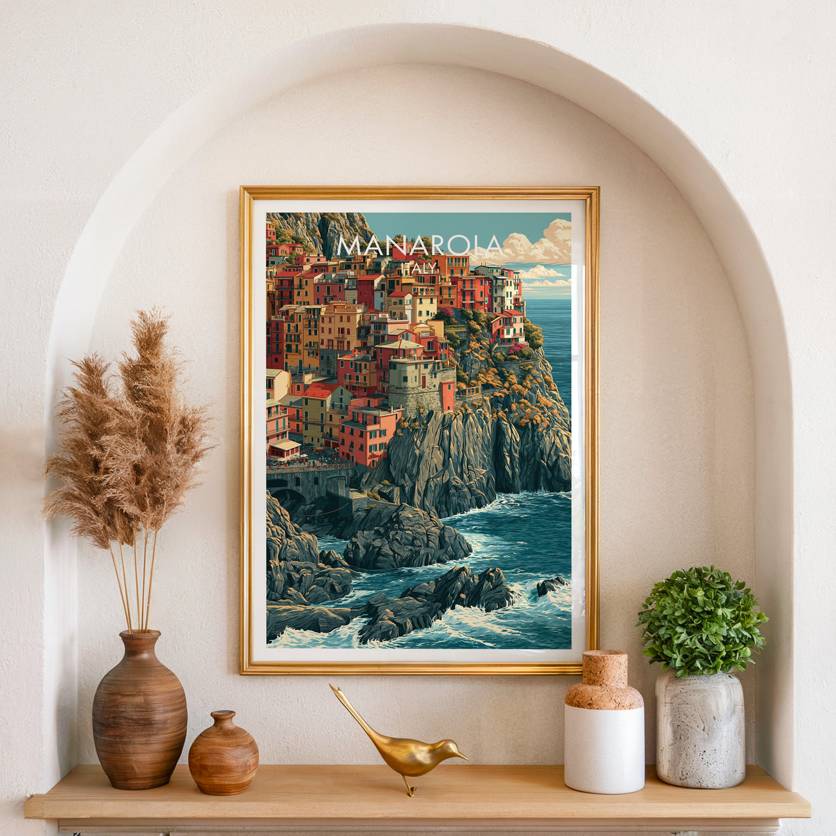 Manarola Cinque Terre print in a gold frame set in an arched plaster alcove with pampas grass and a brass bird