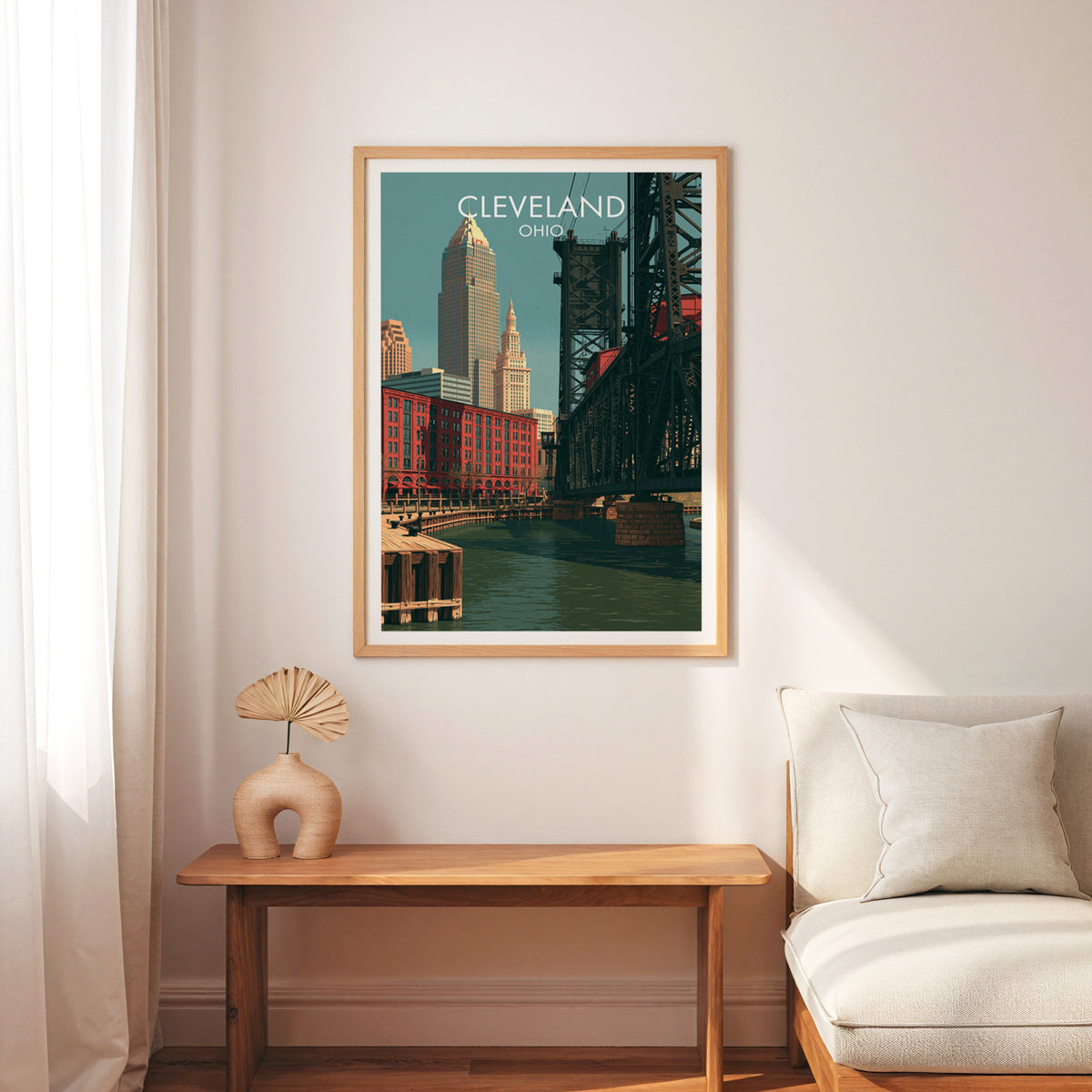 Cleveland travel print in an oak frame above a narrow wooden bench with a cream armchair and palm fan.