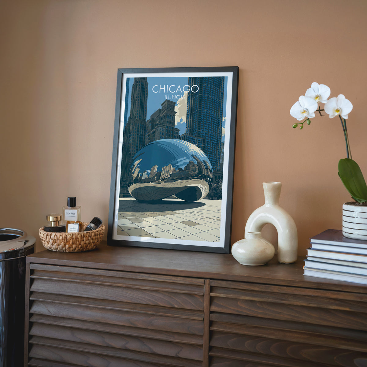 Cloud Gate wall art in a black frame on a walnut sideboard against terracotta, with a cream vase and tray.