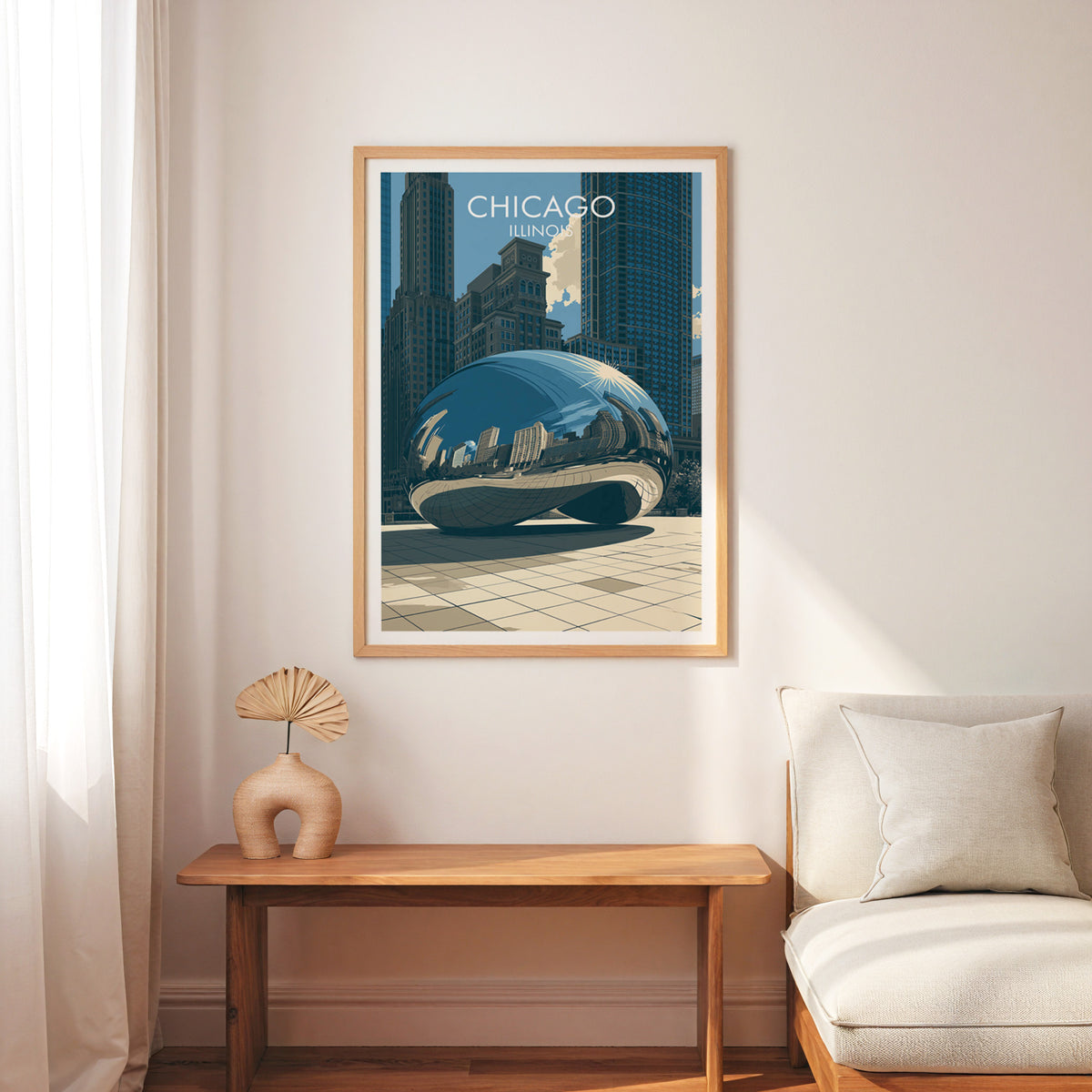 Chicago Bean travel print in an oak frame above a slim wood bench with a cream armchair and palm fan.