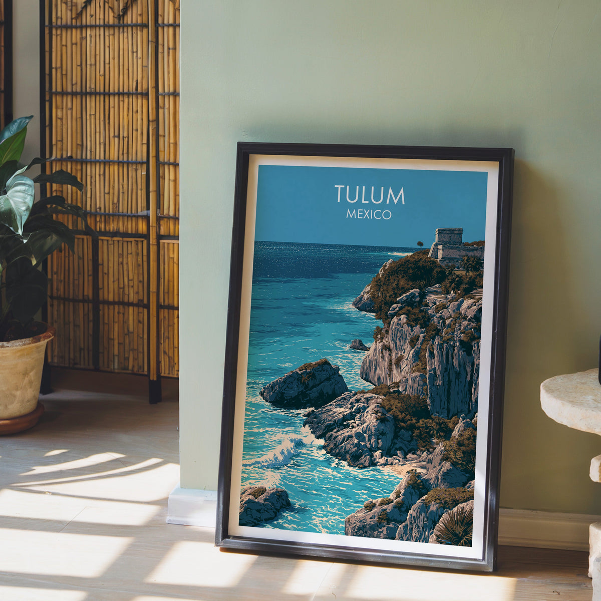 Grey limestone headland print, black frame leaning on a pale wood floor against a sage-green wall.