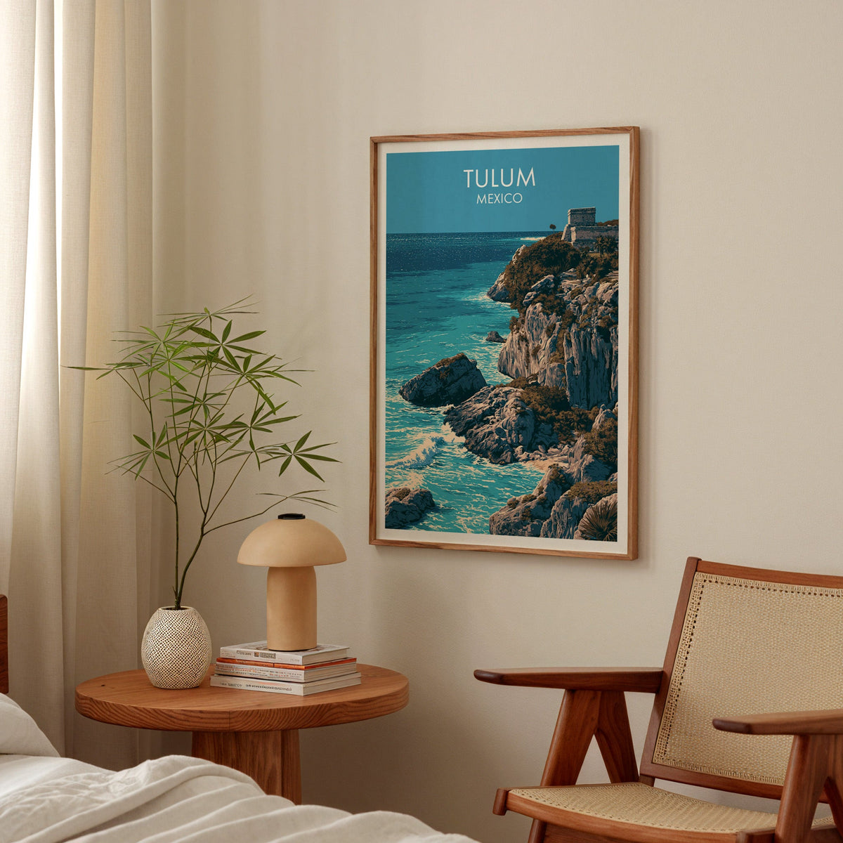 Riviera Maya cliff poster in an oak frame above a bedside table with a mushroom lamp and bamboo stems.