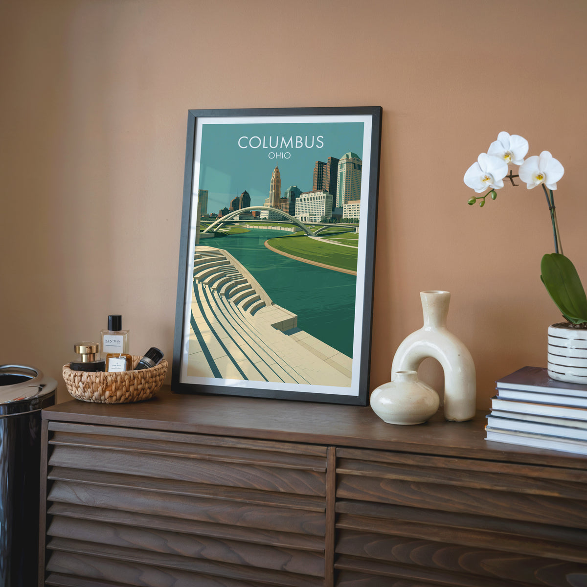 Scioto Mile wall art in a black frame on a walnut sideboard with a terracotta wall and a cream vase.