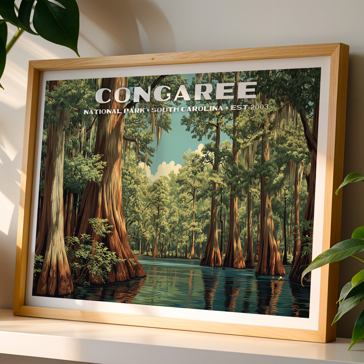 Congaree National Park wall art print in a light oak frame, leaning on a white shelf in warm sunlight beside a monstera plant