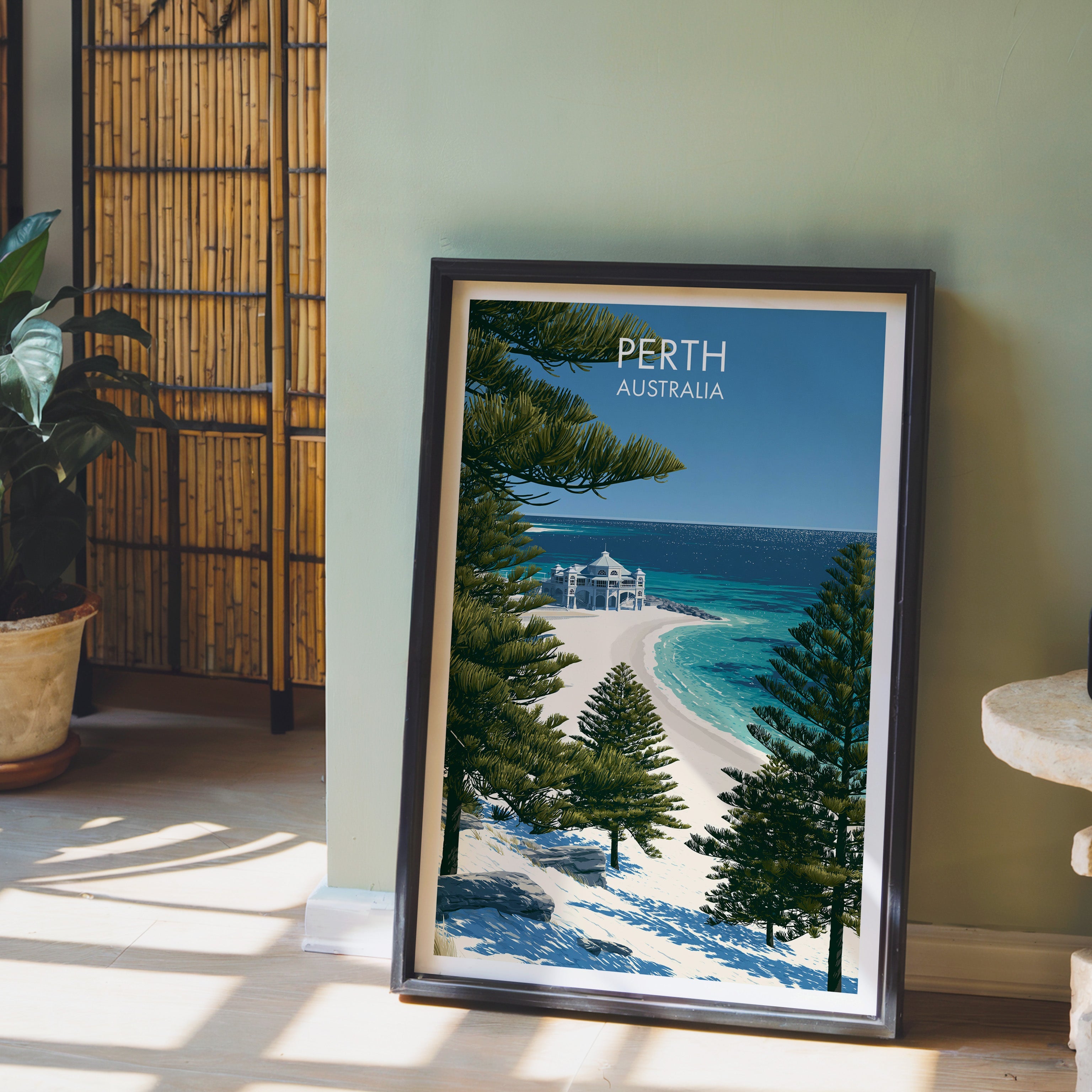 Norfolk pine and beach illustration in a black frame leaning on pale wood floor, sage wall and bamboo screen