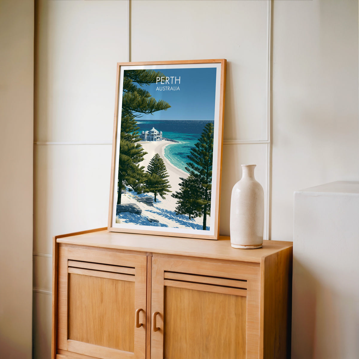 Beach pavilion travel print in an oak frame on a light oak cabinet by a cream panelled wall