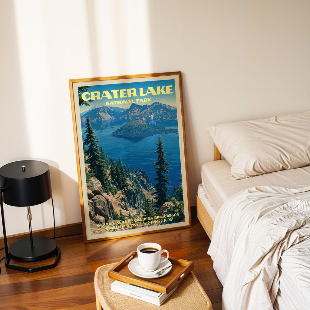 Wizard Island Crater Lake poster in a gold frame on the floor beside a made bed and a black table lamp