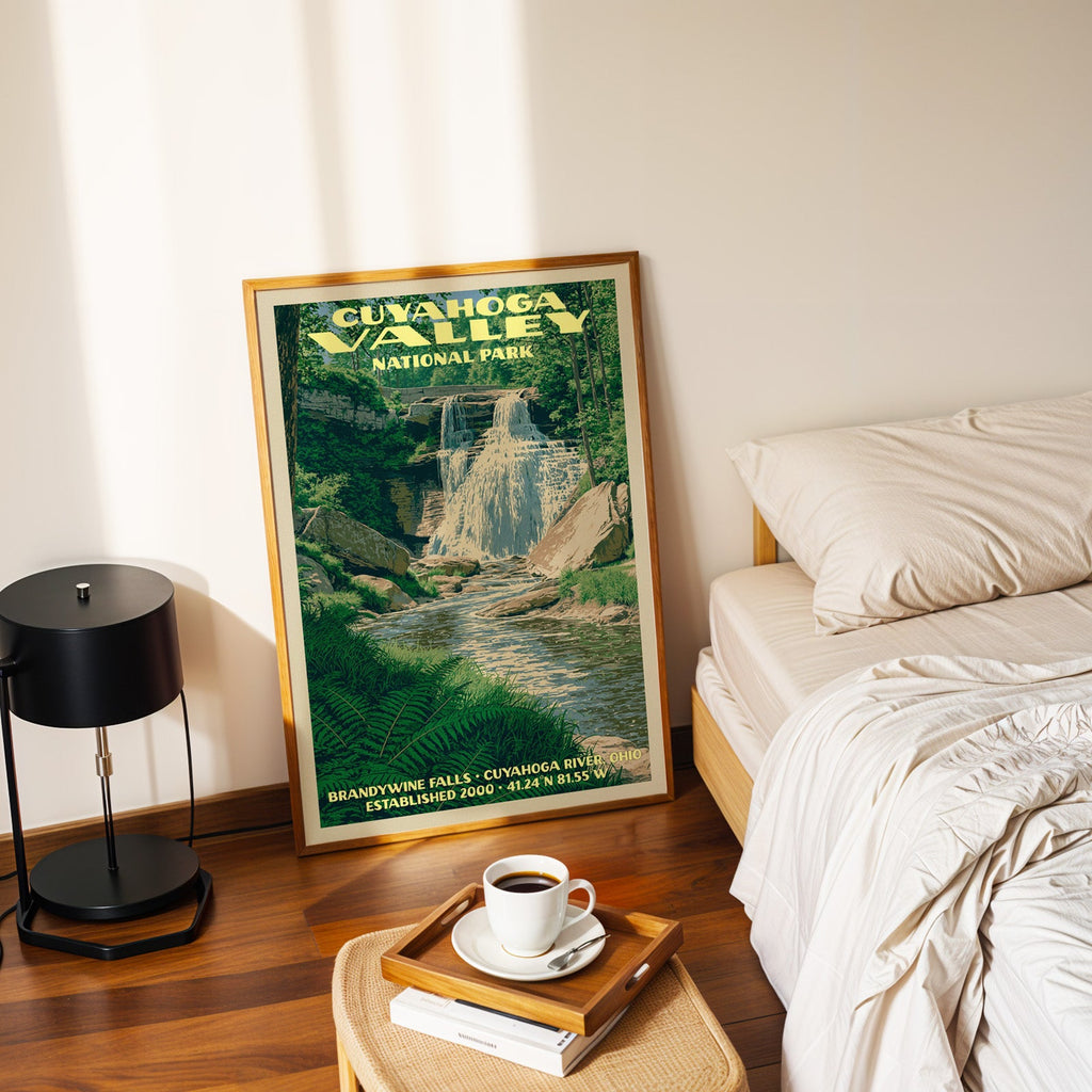 Brandywine Falls Cuyahoga Valley poster in a gold frame on the floor beside a made bed and a black lamp
