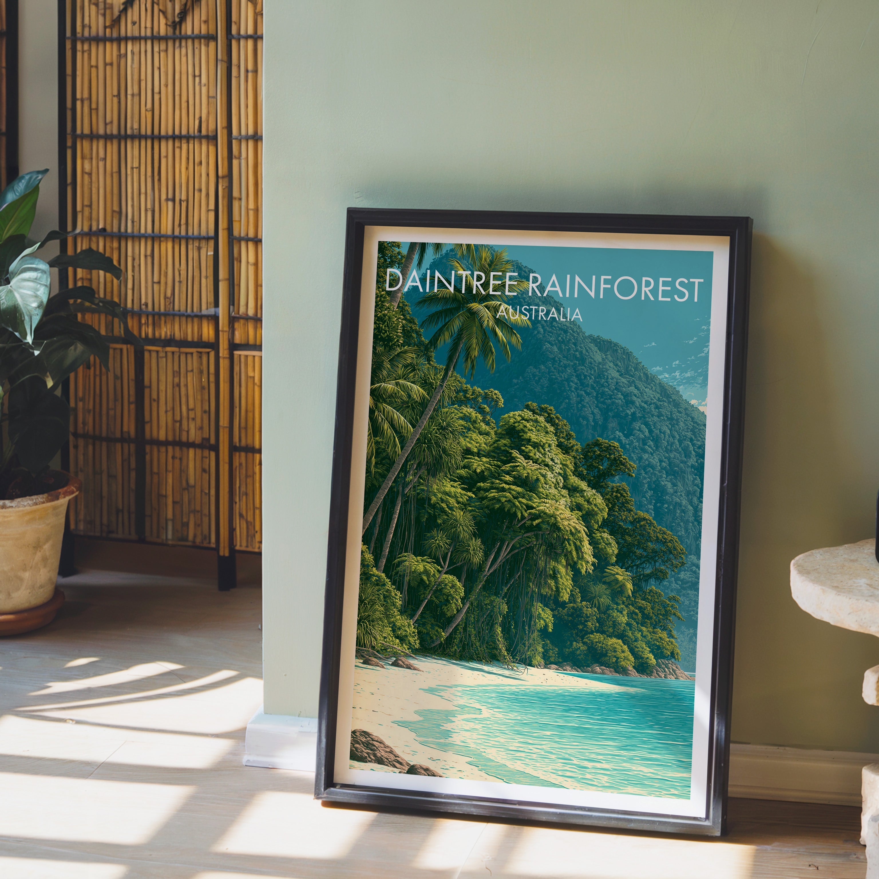 Daintree jungle artwork in a black frame leaning on pale wood floor by a sage-green wall and bamboo screen