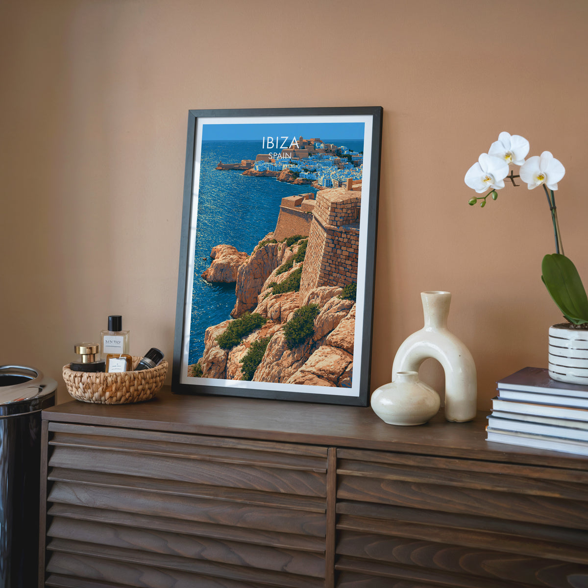 Dalt Vila wall art, black frame on a walnut sideboard against a terracotta wall with a white orchid