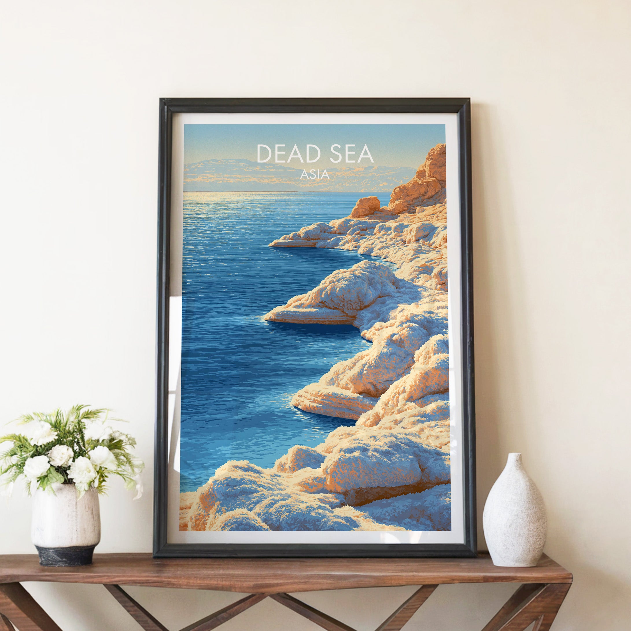 Dead Sea Middle East travel poster in a black frame on a wooden console table with white flowers