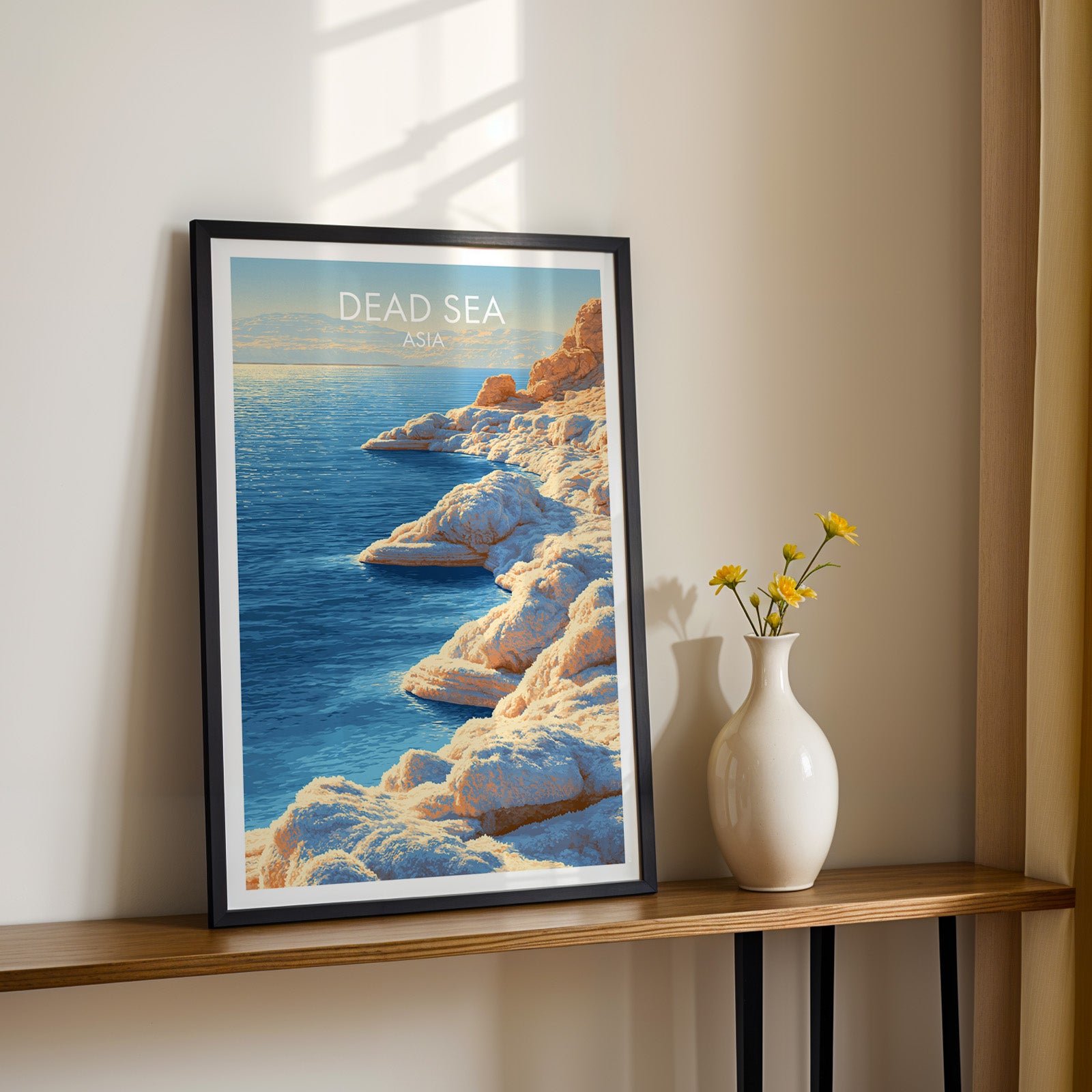 Black framed Dead Sea Middle East print on a narrow hallway console in sunlight, styled with yellow flowers