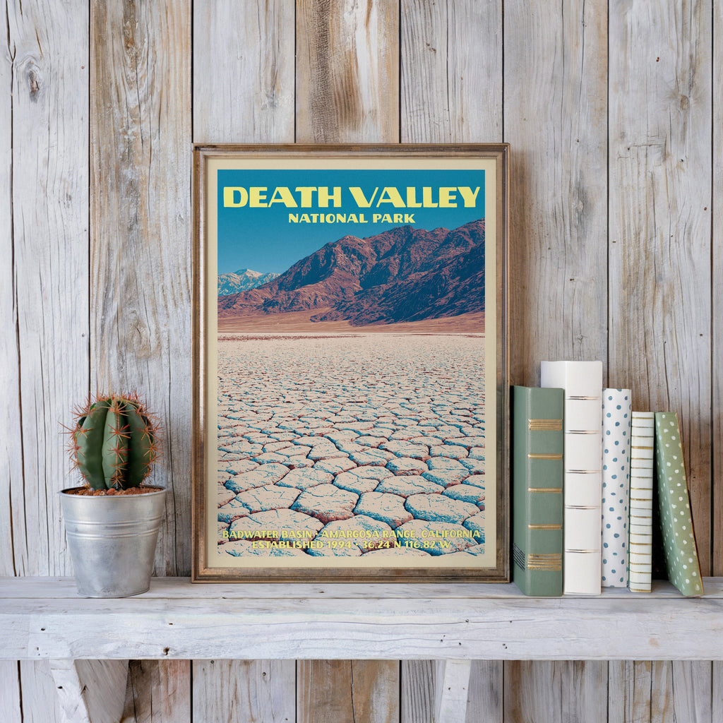 Death Valley vintage poster in a slim gold frame on a whitewashed plank wall beside a cactus and pastel books