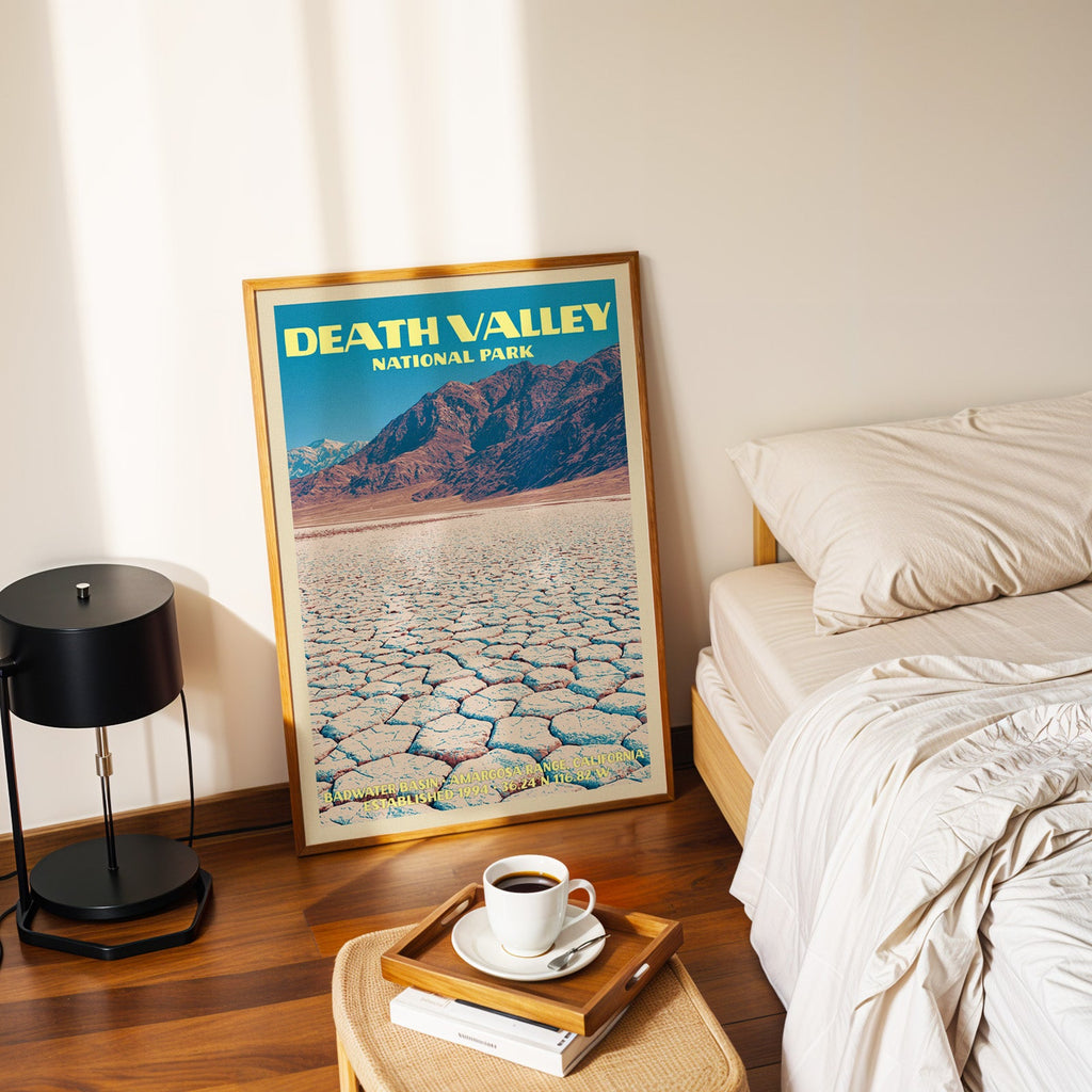 Badwater Basin Death Valley poster in a gold frame on the floor beside a made bed and a black table lamp