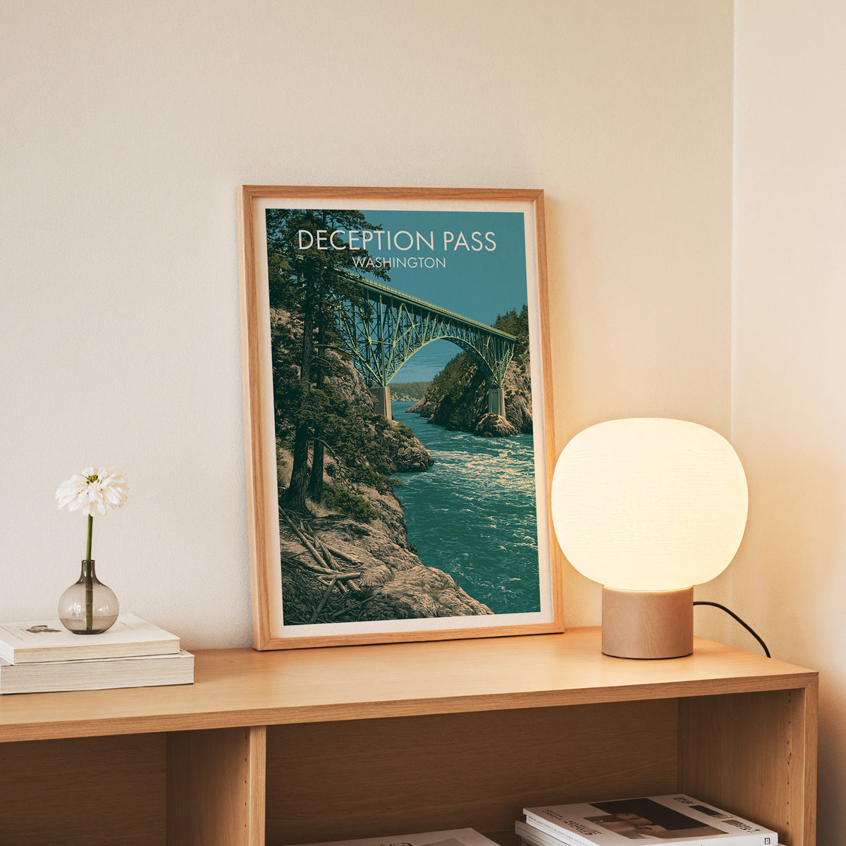 Slim oak frame holding the Deception Pass print on a console with white daisies in a glass jar.