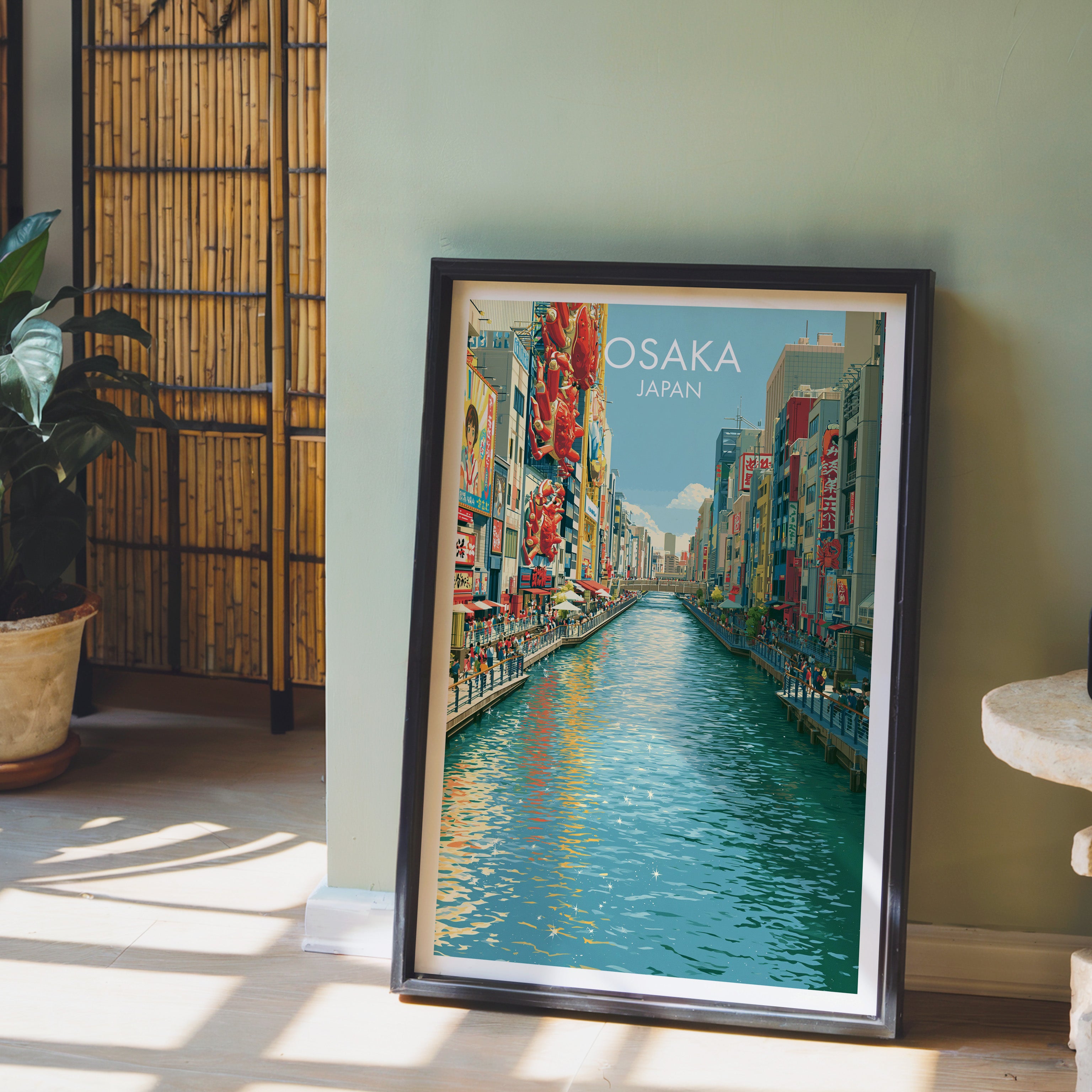 Dotonbori Osaka Japan wall art in a black frame leaning against a sage green wall beside a bamboo screen