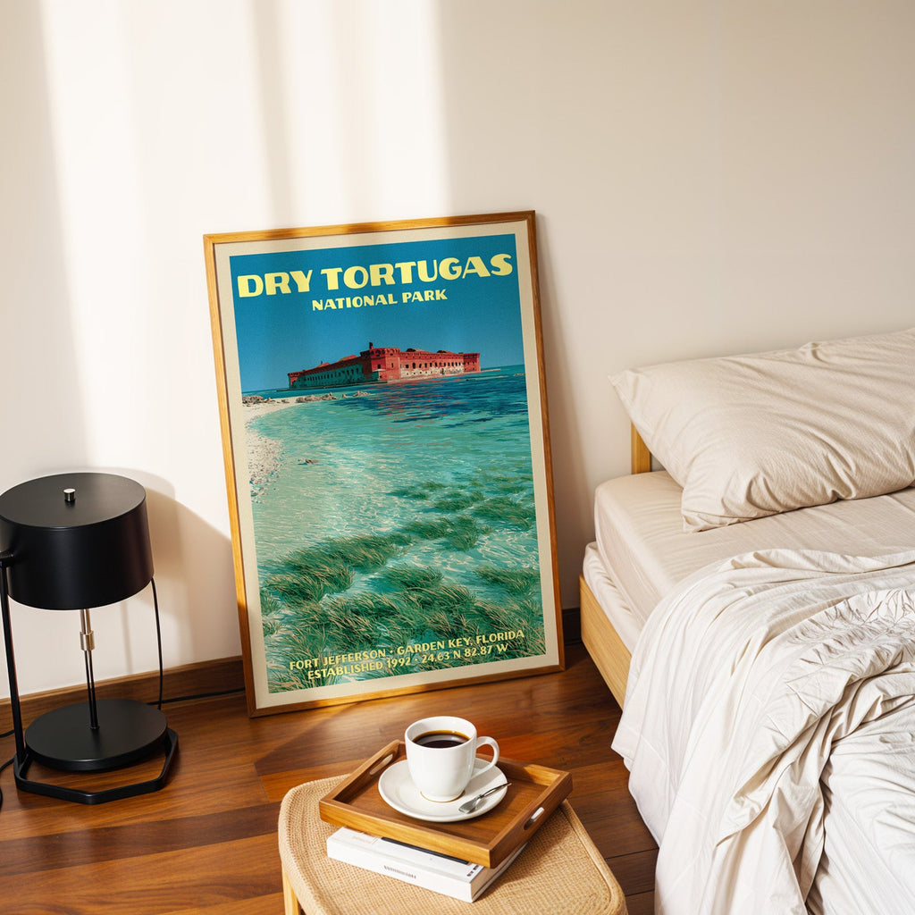 Fort Jefferson Dry Tortugas poster in a gold frame on the floor beside a made bed and a black table lamp