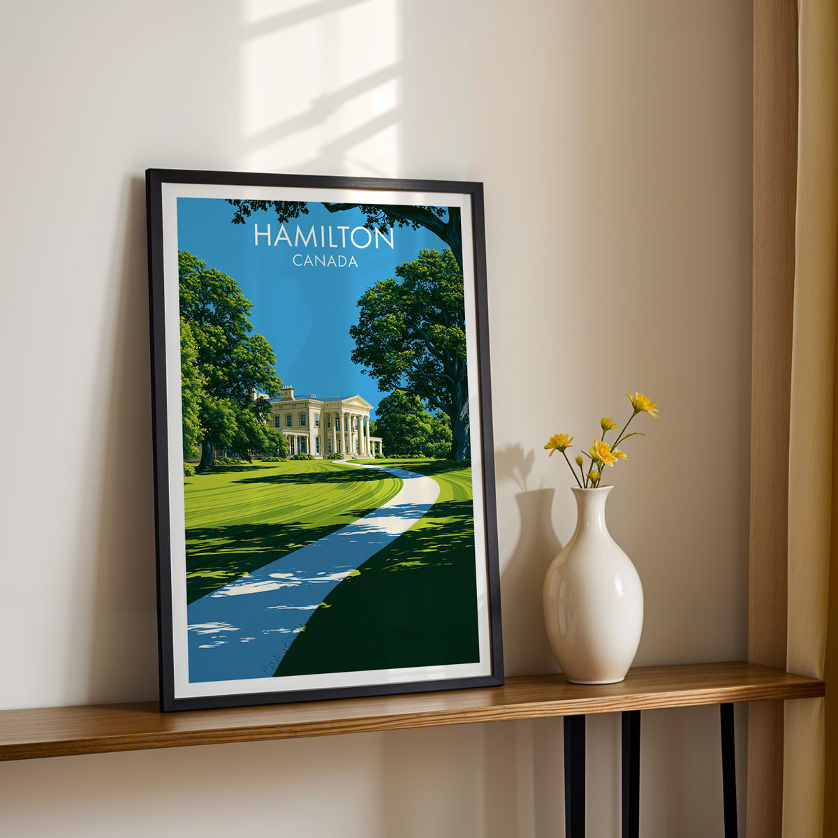 Dundurn Castle garden wall art in a black frame on a sunlit shelf next to yellow daisies