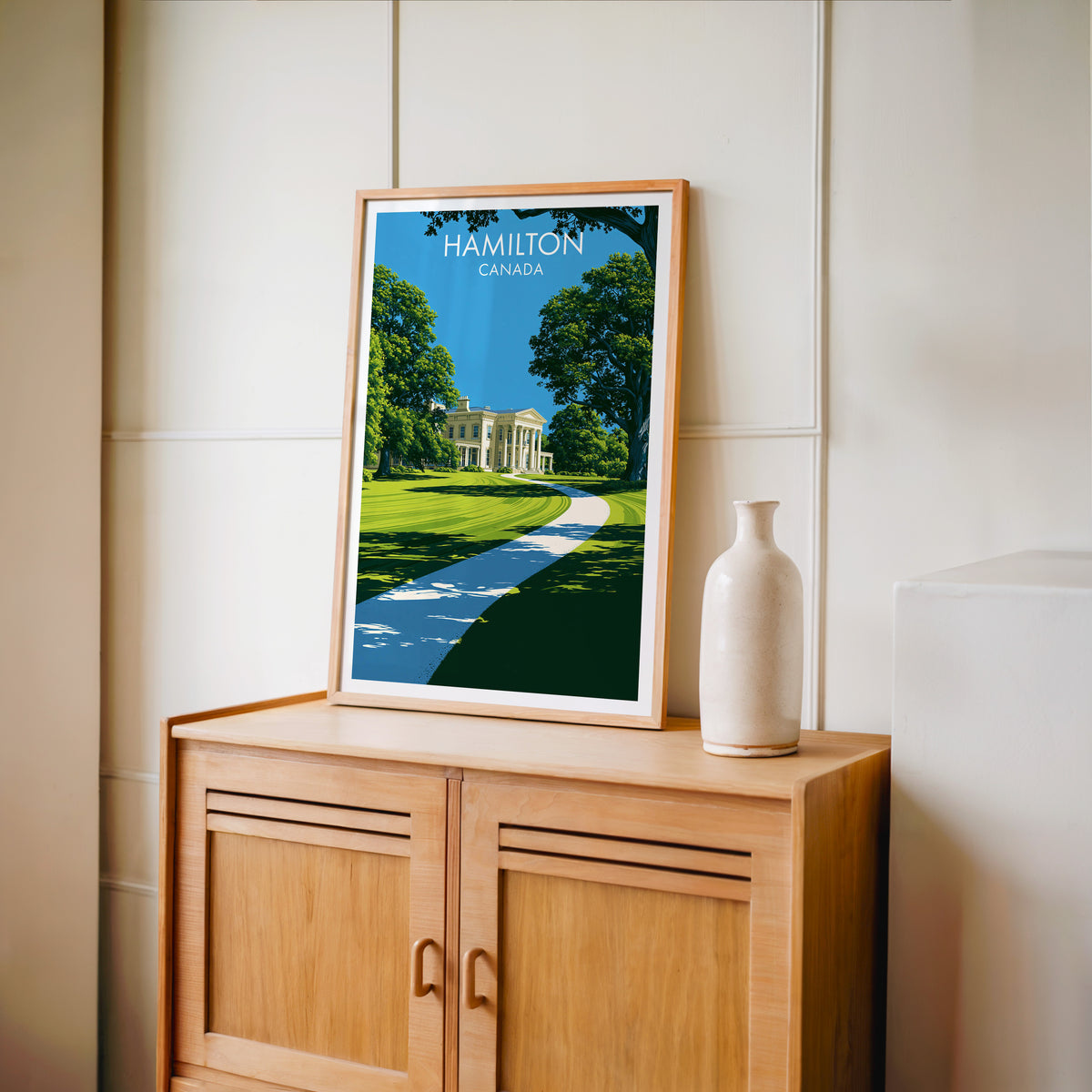 Dundurn Castle garden wall art in an oak frame on a light wood cabinet beside a stoneware vase