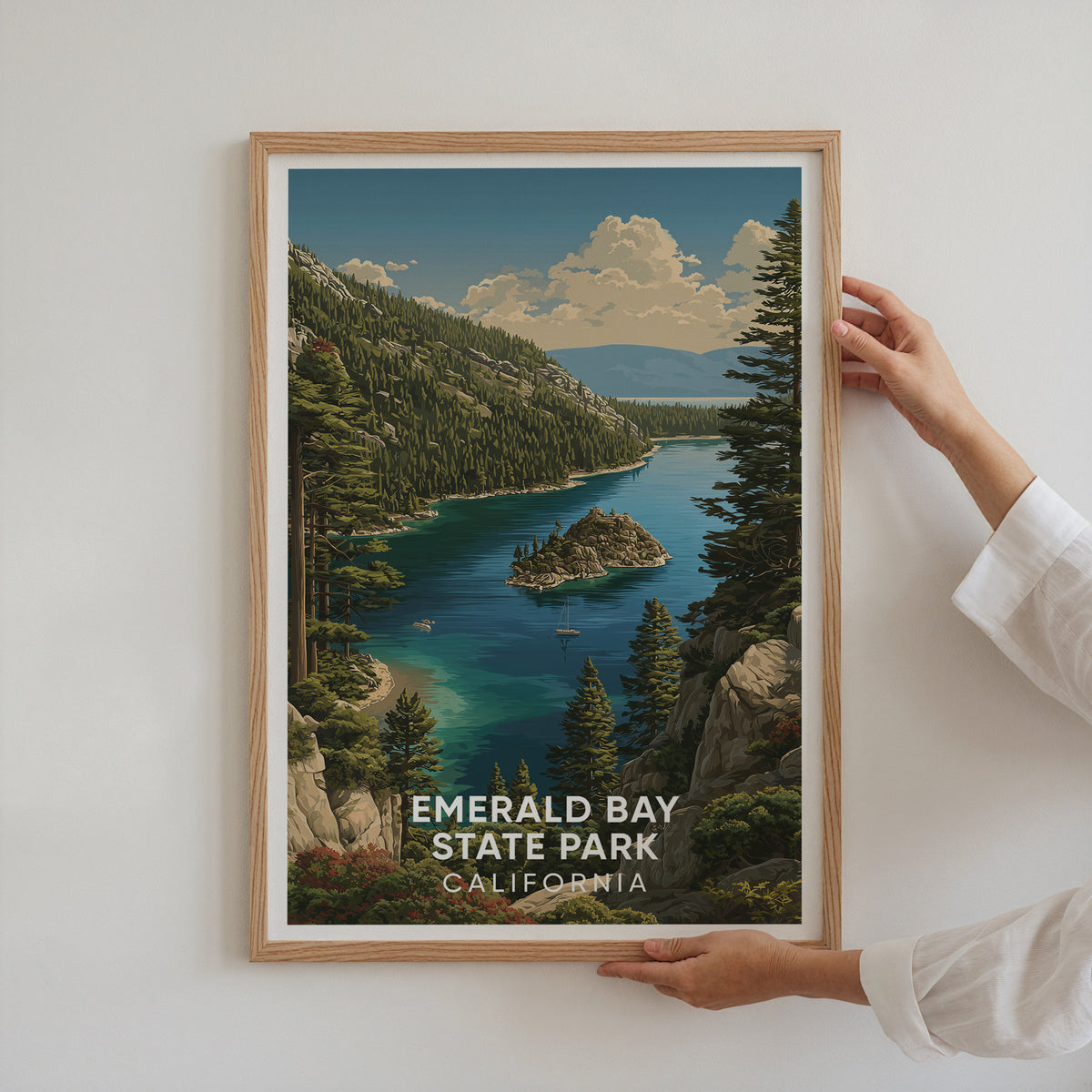 Two hands holding an oak-framed Emerald Bay print against a plain white wall