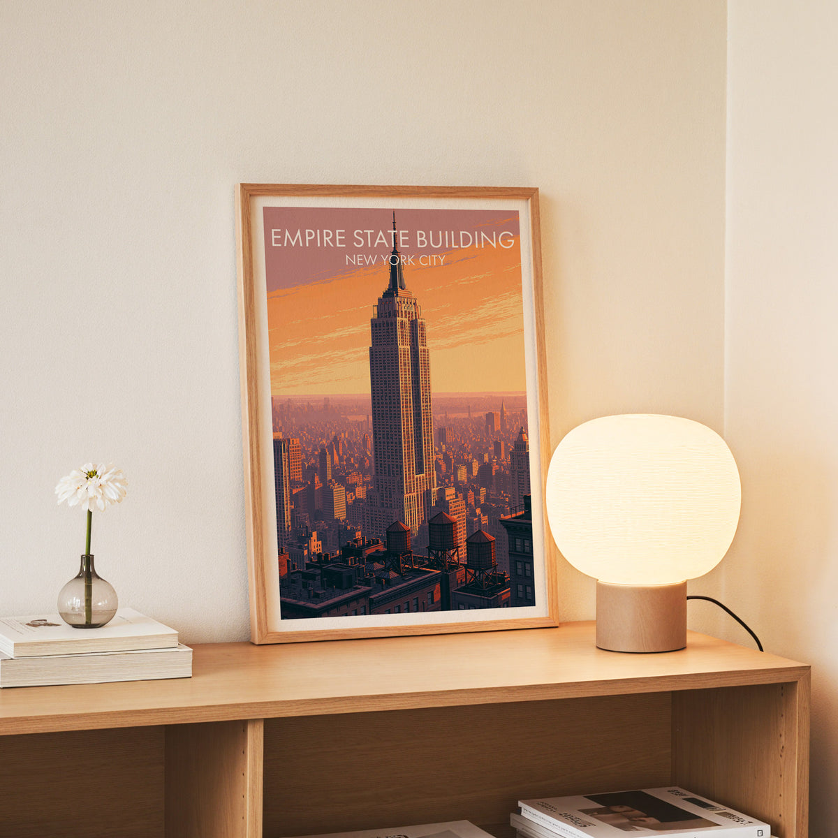 Empire State Building wall art in a slim oak frame on an oak console with daisies in a glass jar.