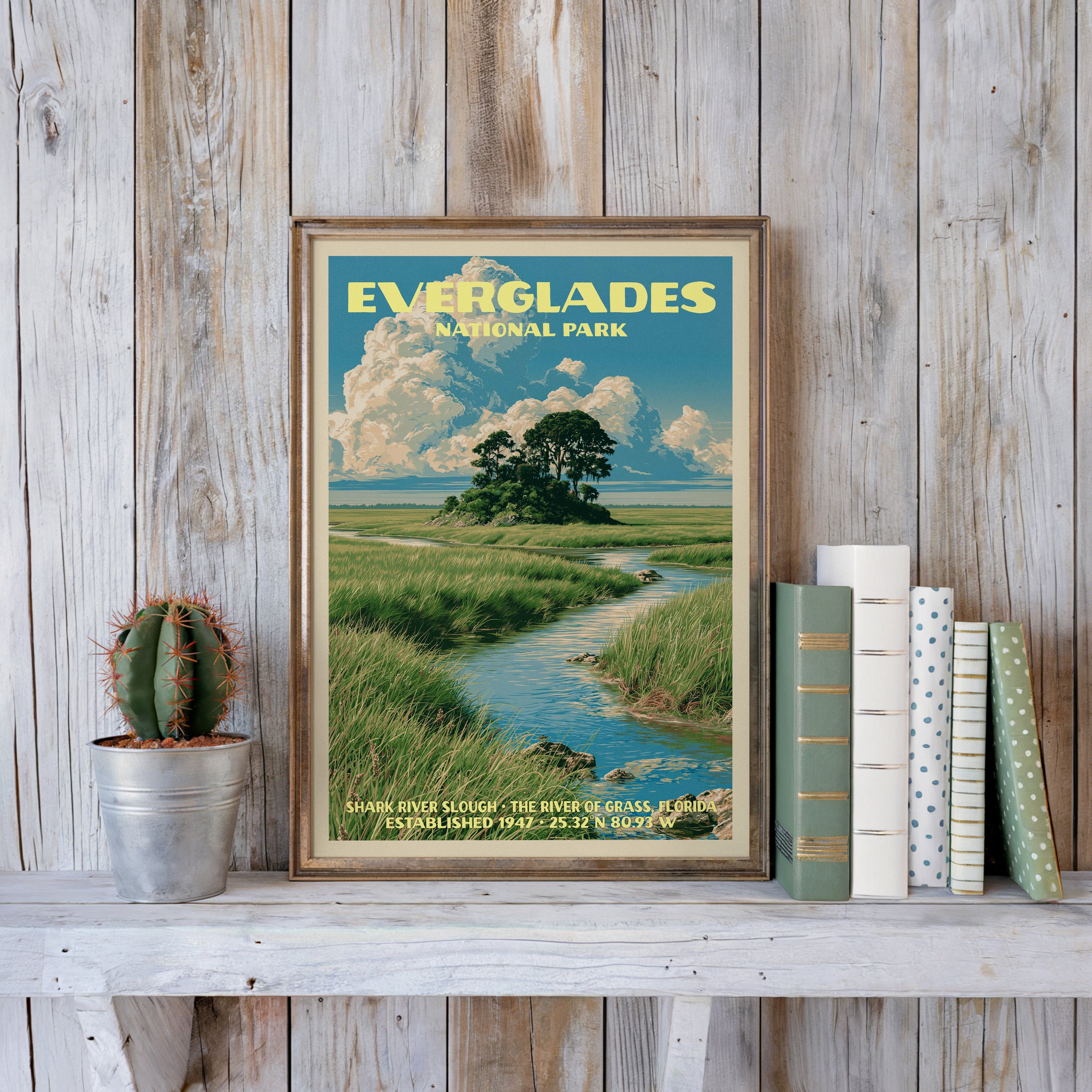 Everglades vintage poster in a slim gold frame on a whitewashed plank wall beside a tin-potted cactus and books