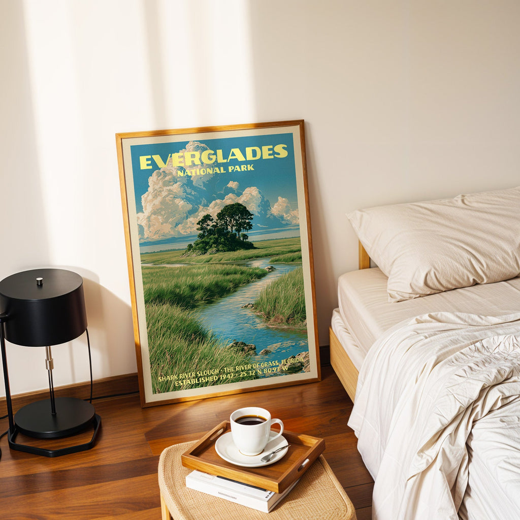 Shark River Slough Everglades poster in a gold frame on the floor beside a made bed and a black table lamp
