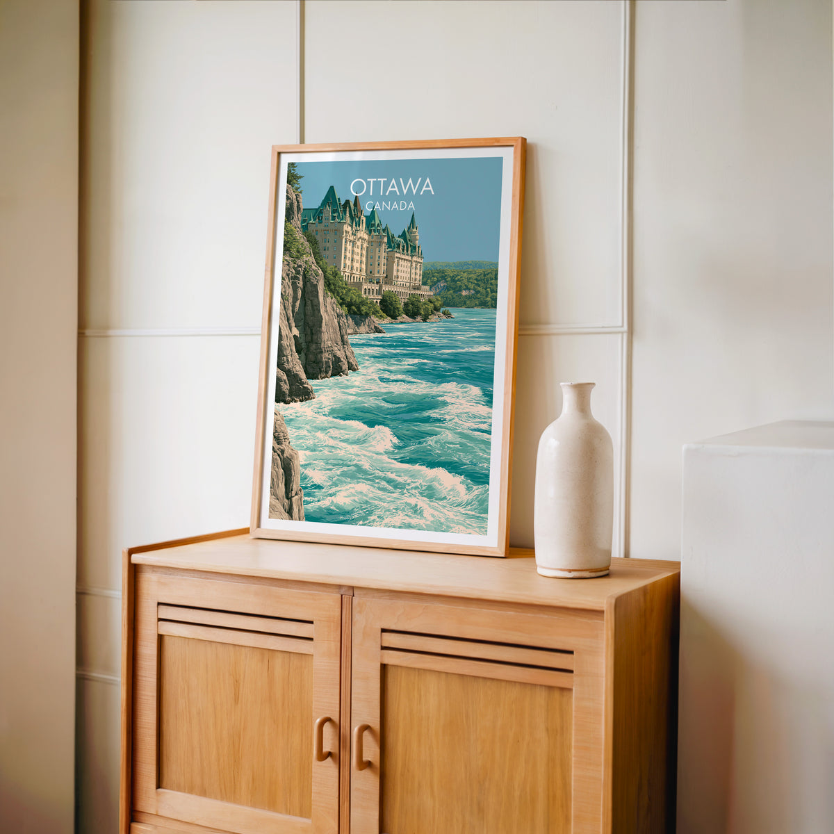 Chateau Laurier copper roof art in an oak frame on a light wood cabinet beside a stoneware vase