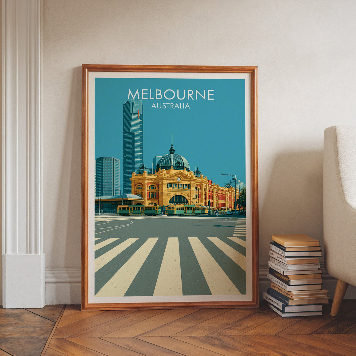 Melbourne travel artwork in a walnut frame leaning on herringbone floor beside book stacks and a pale armchair