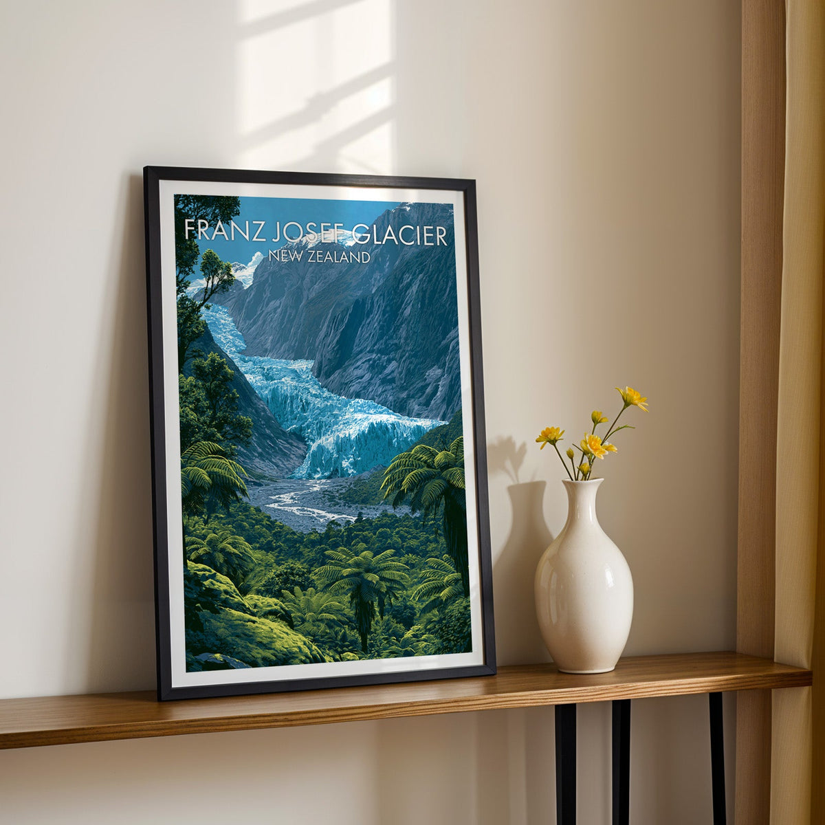 Blue ice and fern artwork, black frame on a wood shelf with yellow daisies against a sunlit cream wall