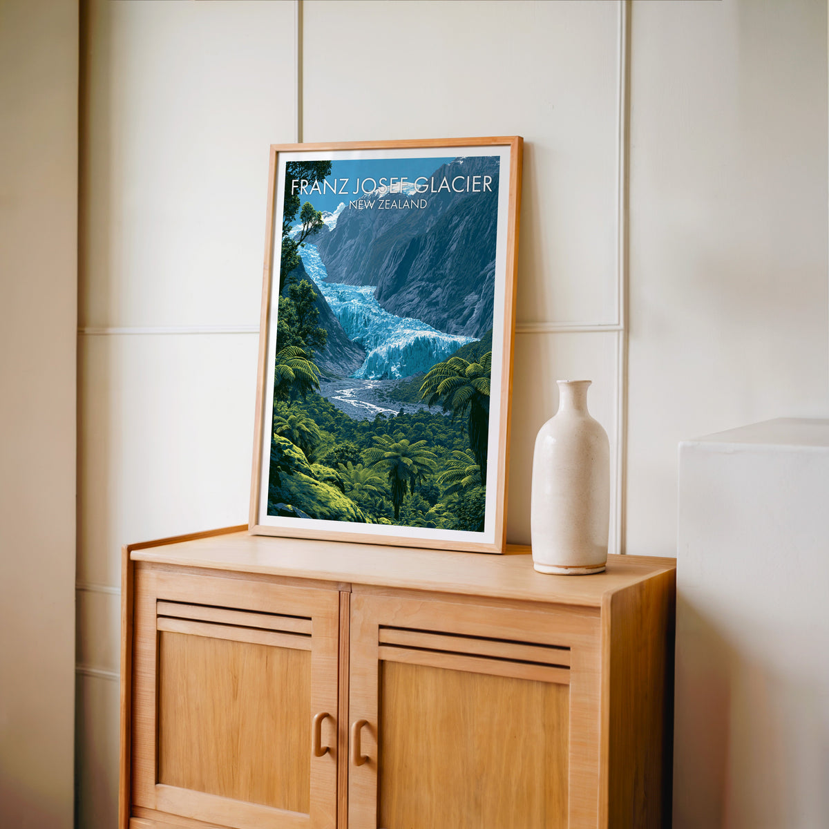West Coast glacier poster in an oak frame on a light oak cabinet beside a pale bottle vase