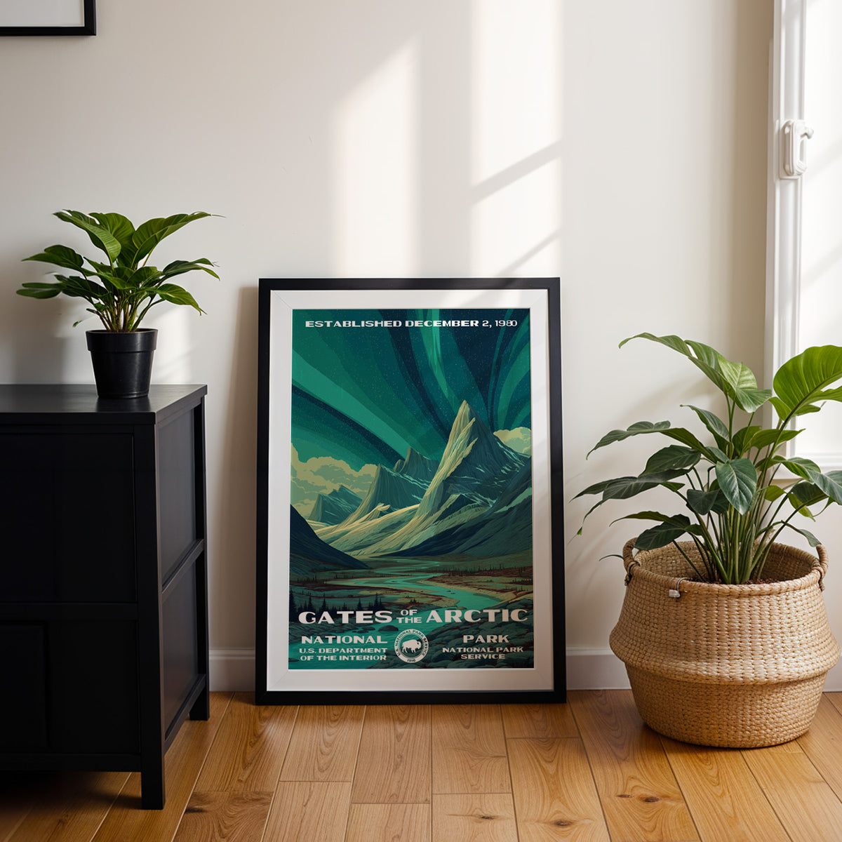 Gates of the Arctic National Park travel poster in a black frame leaning by a dark cabinet and plants