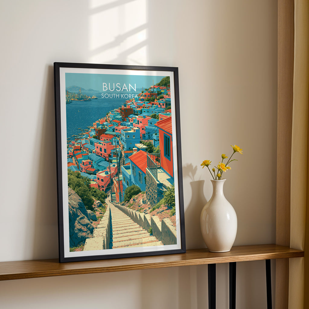Black framed Gamcheon Culture Village Busan print on a narrow hallway console in sunlight, styled with yellow flowers