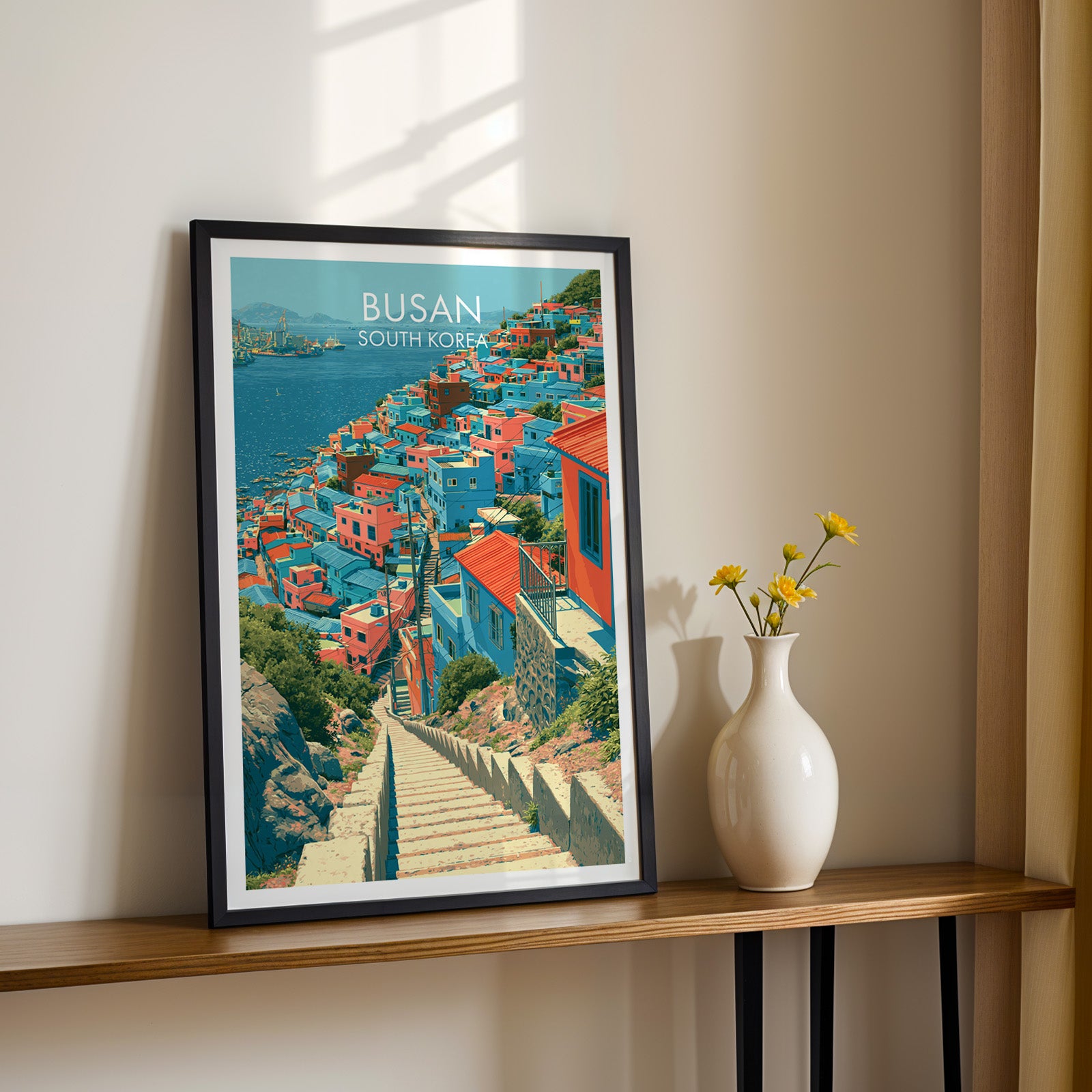 Black framed Gamcheon Culture Village Busan print on a narrow hallway console in sunlight, styled with yellow flowers