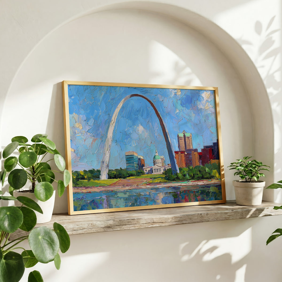 Gateway Arch oil painting wall art in a gold frame on a wood shelf with potted plants