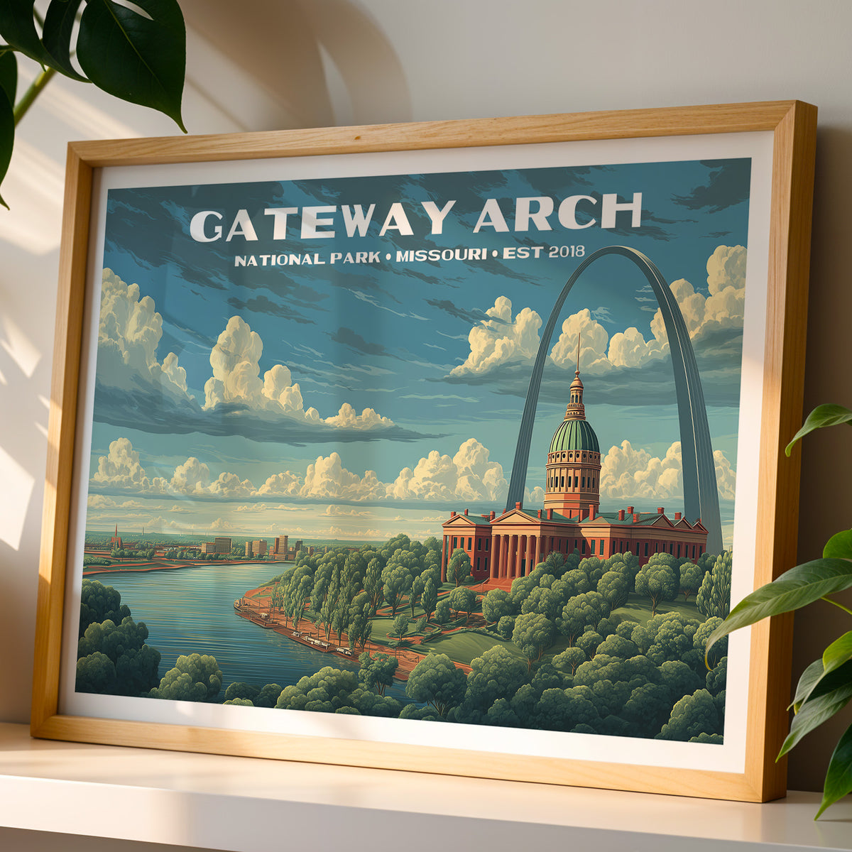 Gateway Arch National Park wall art print in a light oak frame, leaning on a white shelf in warm sunlight beside a monstera plant