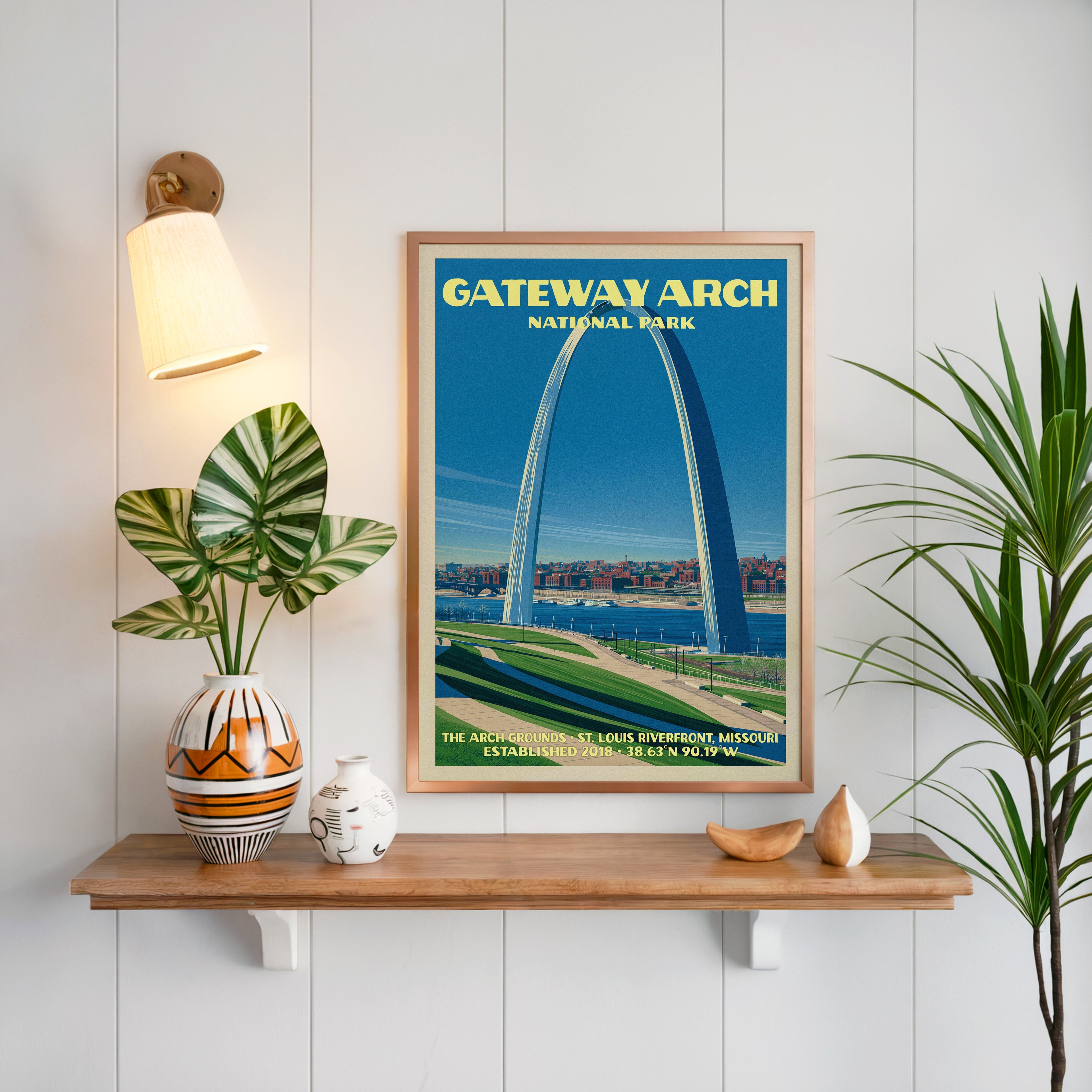 St. Louis Gateway Arch print framed on white panelling above an oak shelf with a patterned vase and sconce
