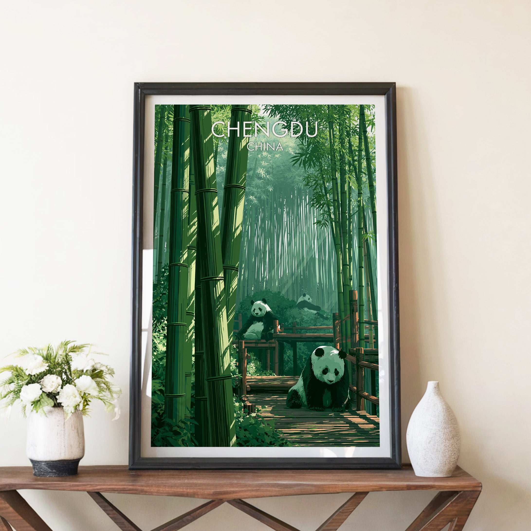 Giant Pandas Chengdu China travel poster in a black frame on a wooden console table with white flowers